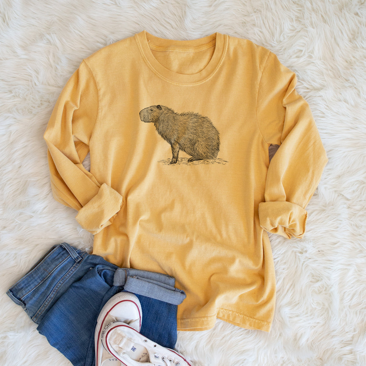 Golden wheat yellow Comfort Colors long sleeve shirt printed with a detailed black ink illustration of a capybara standing in profile, shown in a lifestyle photo.