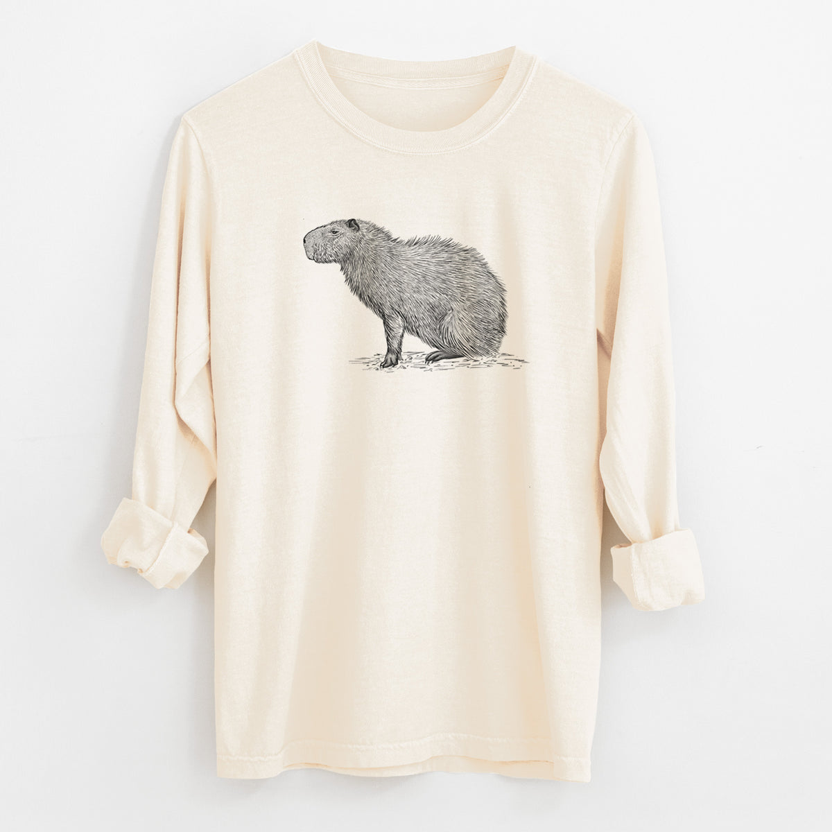Ivory Comfort Colors long sleeve shirt laid flat with the cuffs rolled, printed with a detailed black ink illustration of a capybara standing in profile.
