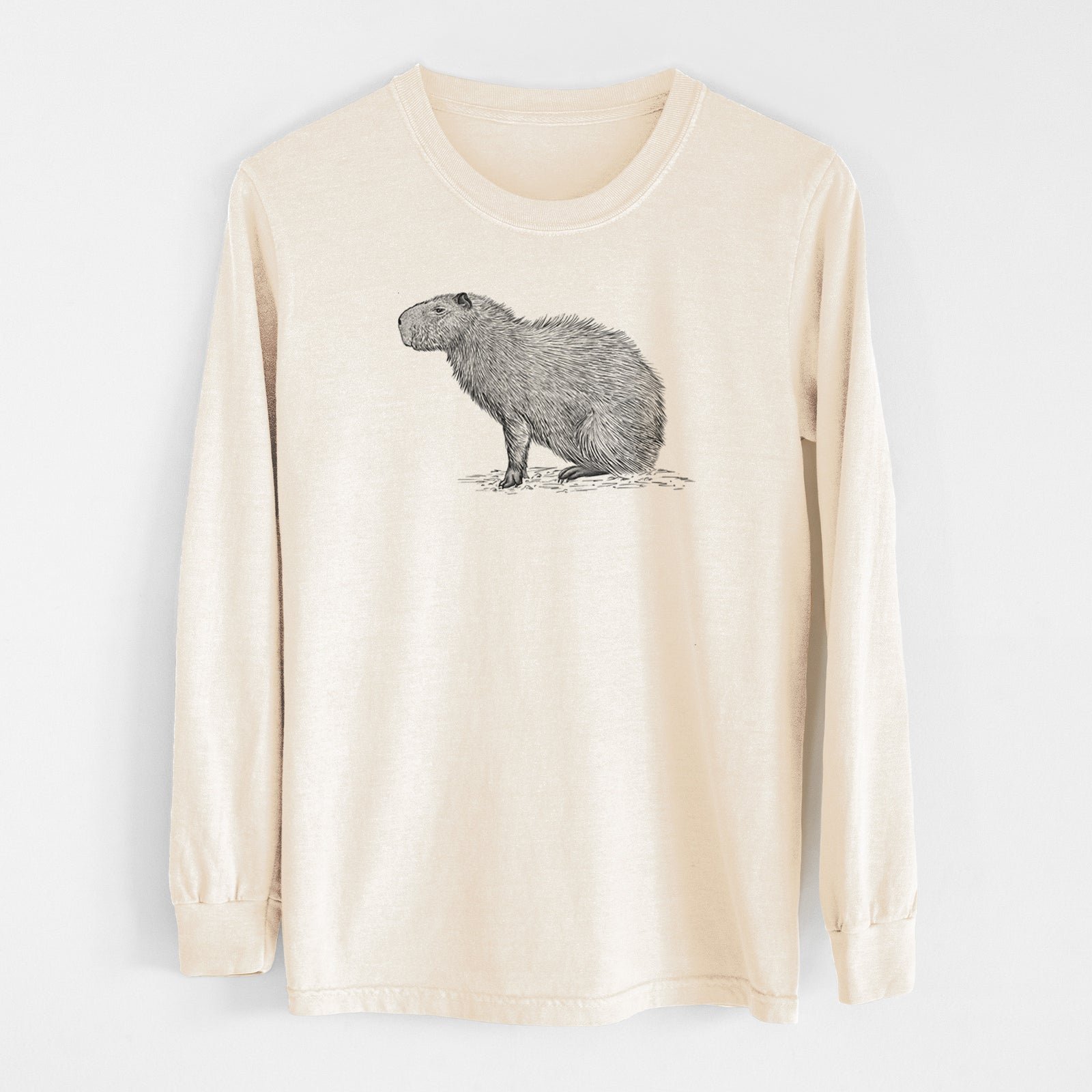 Ivory Comfort Colors long sleeve shirt laid flat, printed with a detailed black ink illustration of a capybara standing in profile.