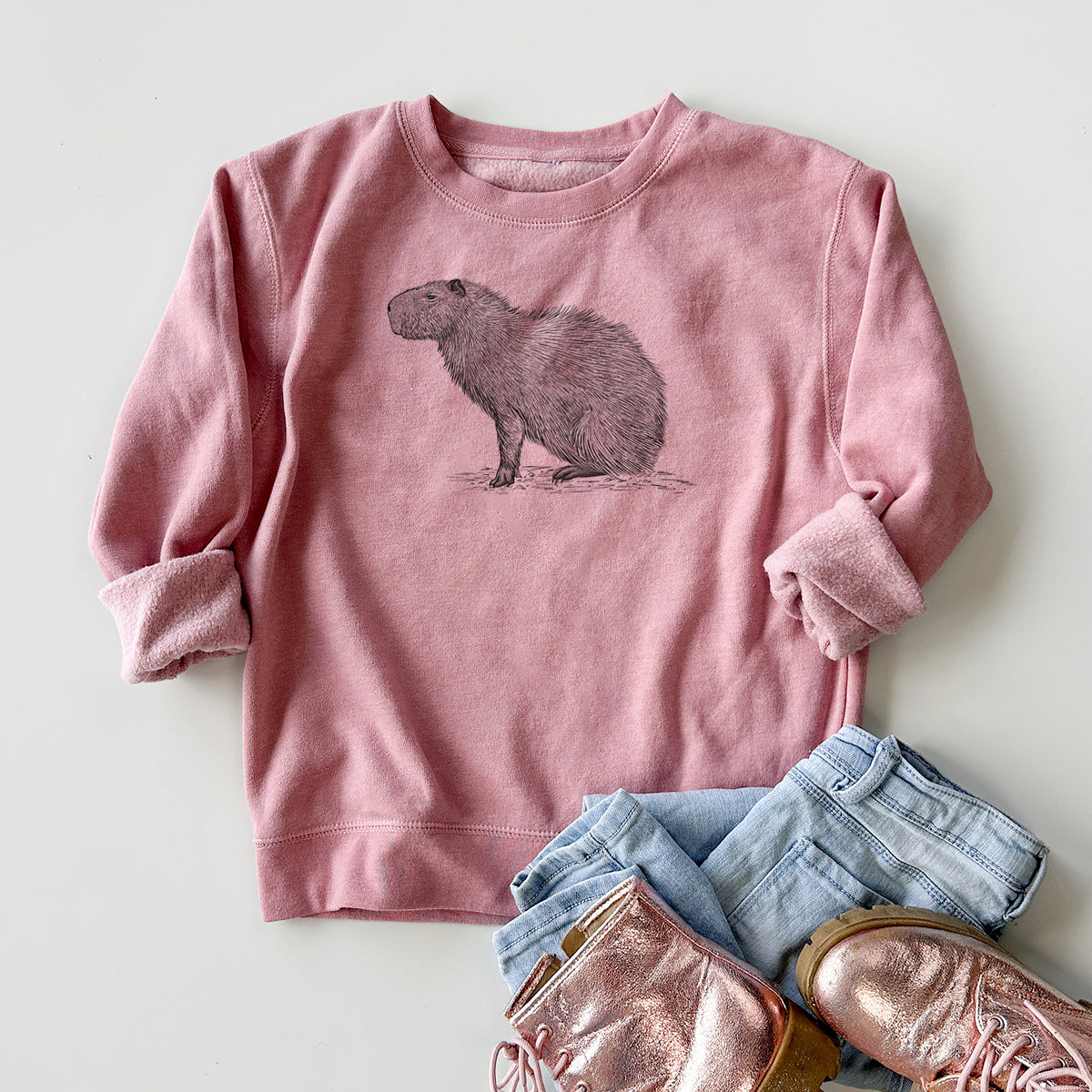 Youth crewneck sweatshirt printed with a detailed black ink illustration of a capybara standing in profile, styled flat with jeans and boots.