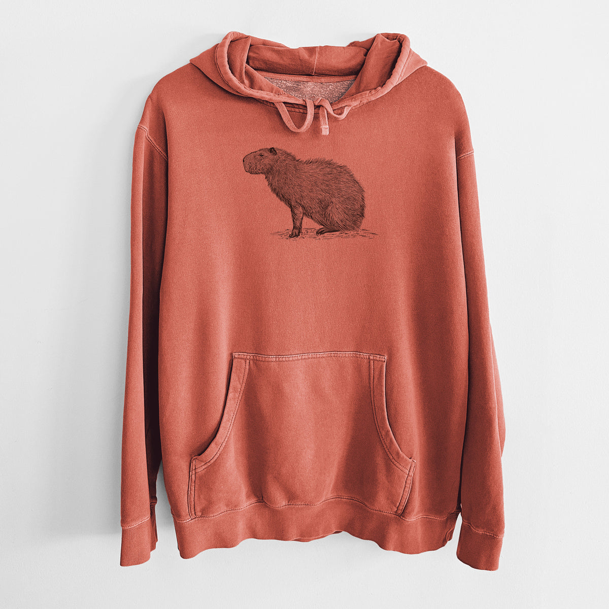 Amber orange pigment dyed hoodie laid flat, printed with a detailed black ink illustration of a capybara standing in profile.