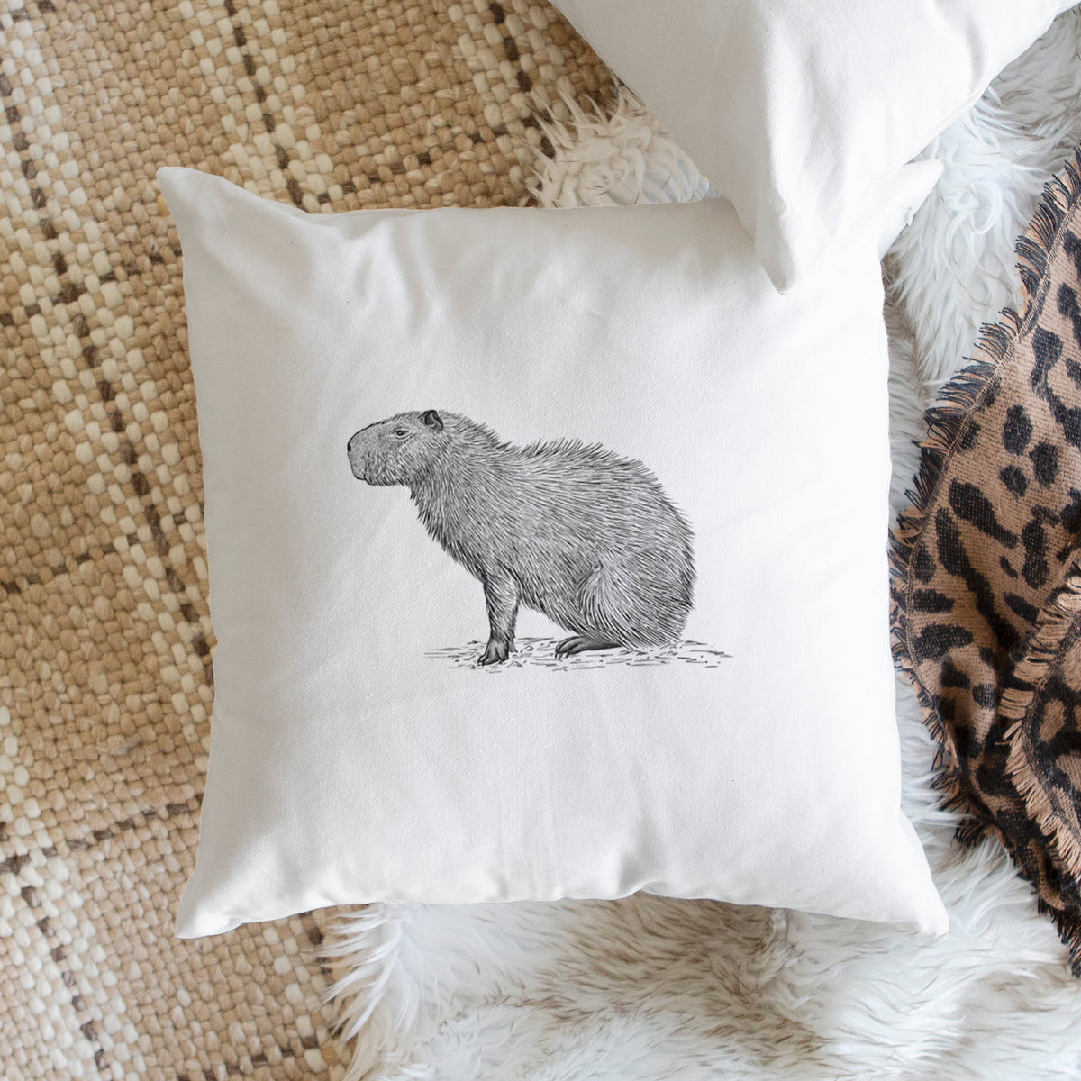 White pillow cover printed with a detailed black ink illustration of a capybara standing in profile, on a woven chair.