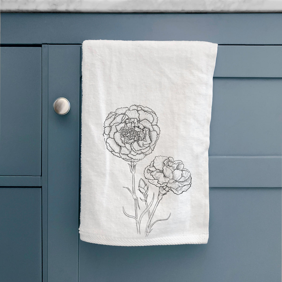 White hand towel printed with a black ink line drawing of carnation flowers on stems, hanging on a cabinet door.