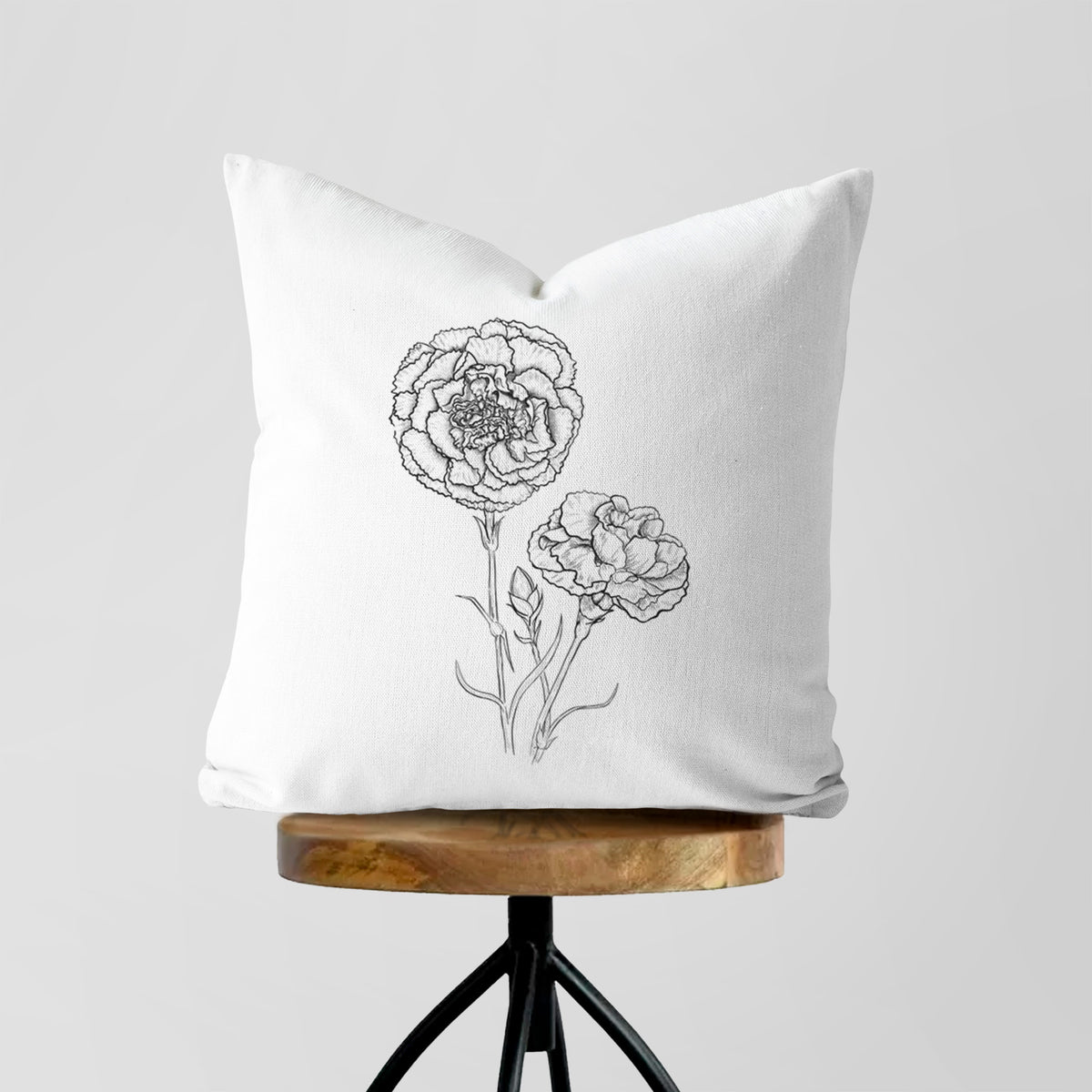 White pillow cover printed with a black ink line drawing of carnation flowers on stems, on a wooden stool.