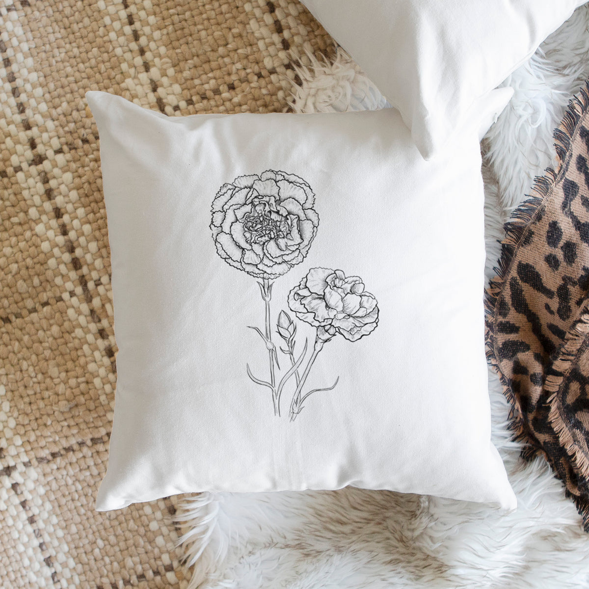 White pillow cover printed with a black ink line drawing of carnation flowers on stems, on a woven chair.