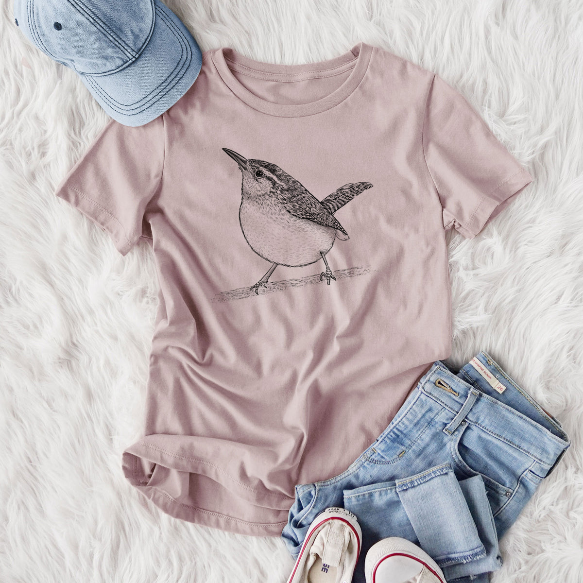 Women's relaxed fit cotton t-shirt printed with a detailed black ink sketch of a Carolina wren perched on a branch with its tail raised, styled flat on a white faux fur rug with jeans.