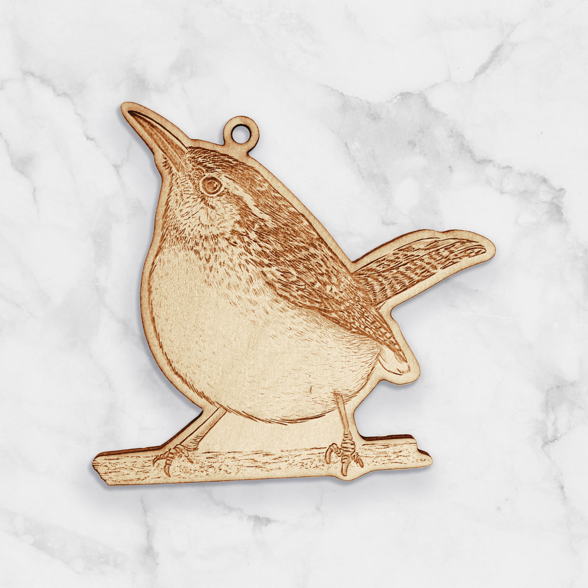 Wooden ornament featuring a detailed engraving of a Carolina wren perched on a branch with its tail raised, on a marble surface.