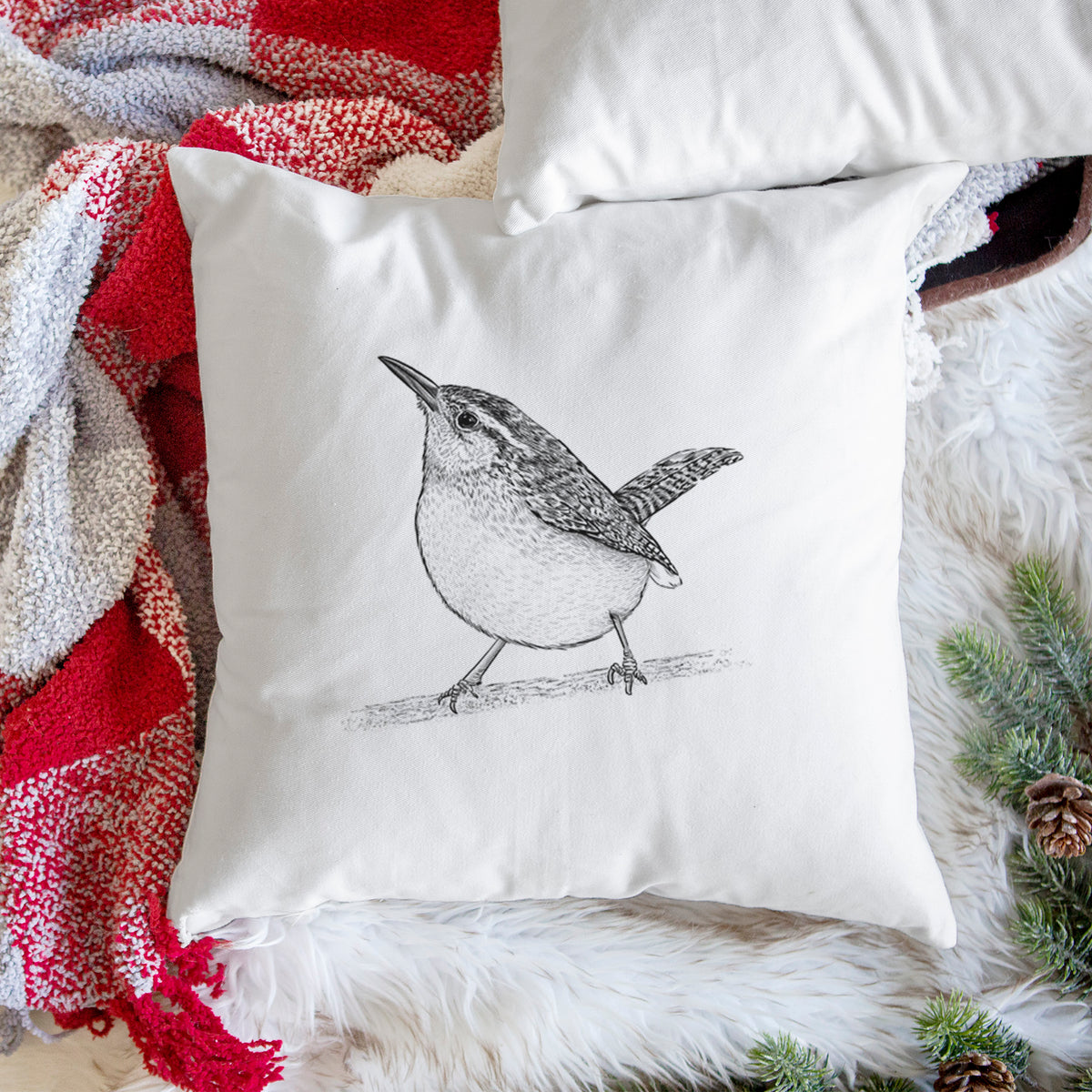 White pillow cover printed with a detailed black ink sketch of a Carolina wren perched on a branch with its tail raised, on a woven chair.