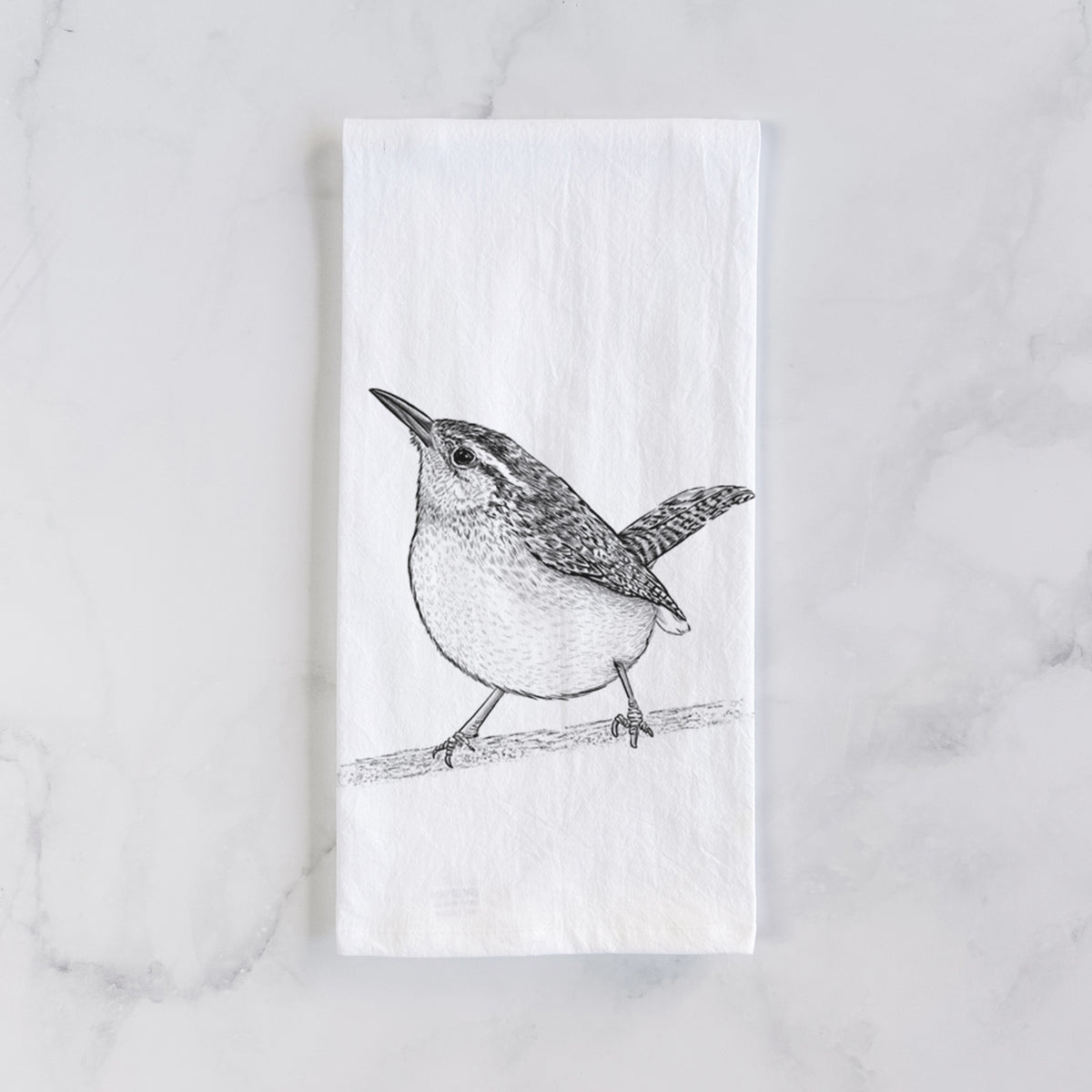 White cotton tea towel laid flat on marble, printed with a detailed black ink sketch of a Carolina wren perched on a branch with its tail raised.