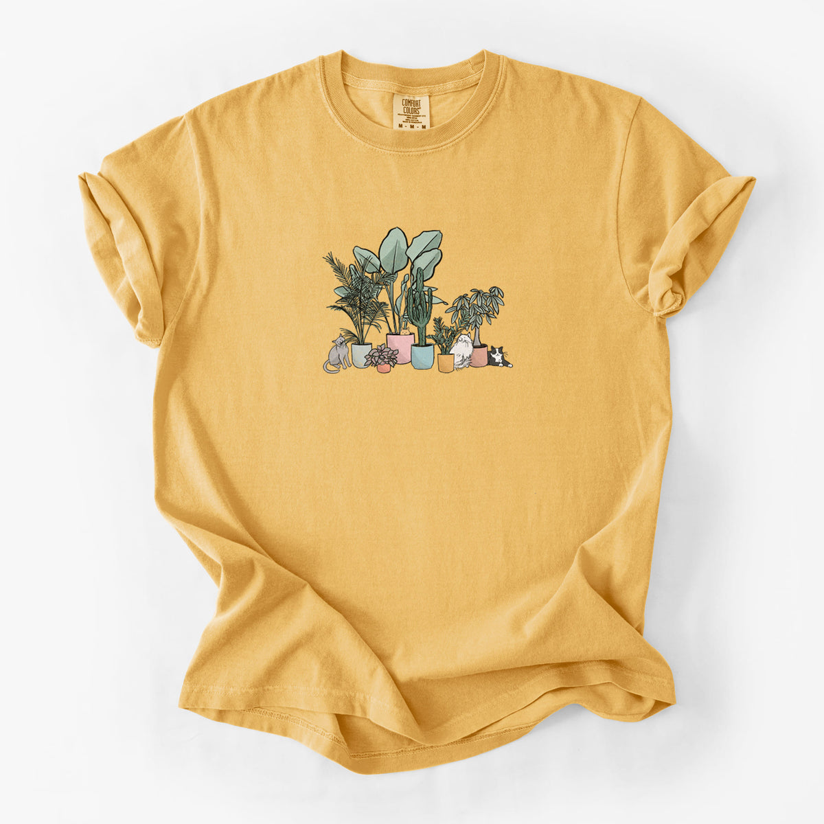 Golden wheat yellow Comfort Colors t-shirt laid flat, printed with a full-color illustration of cats lounging among potted houseplants.
