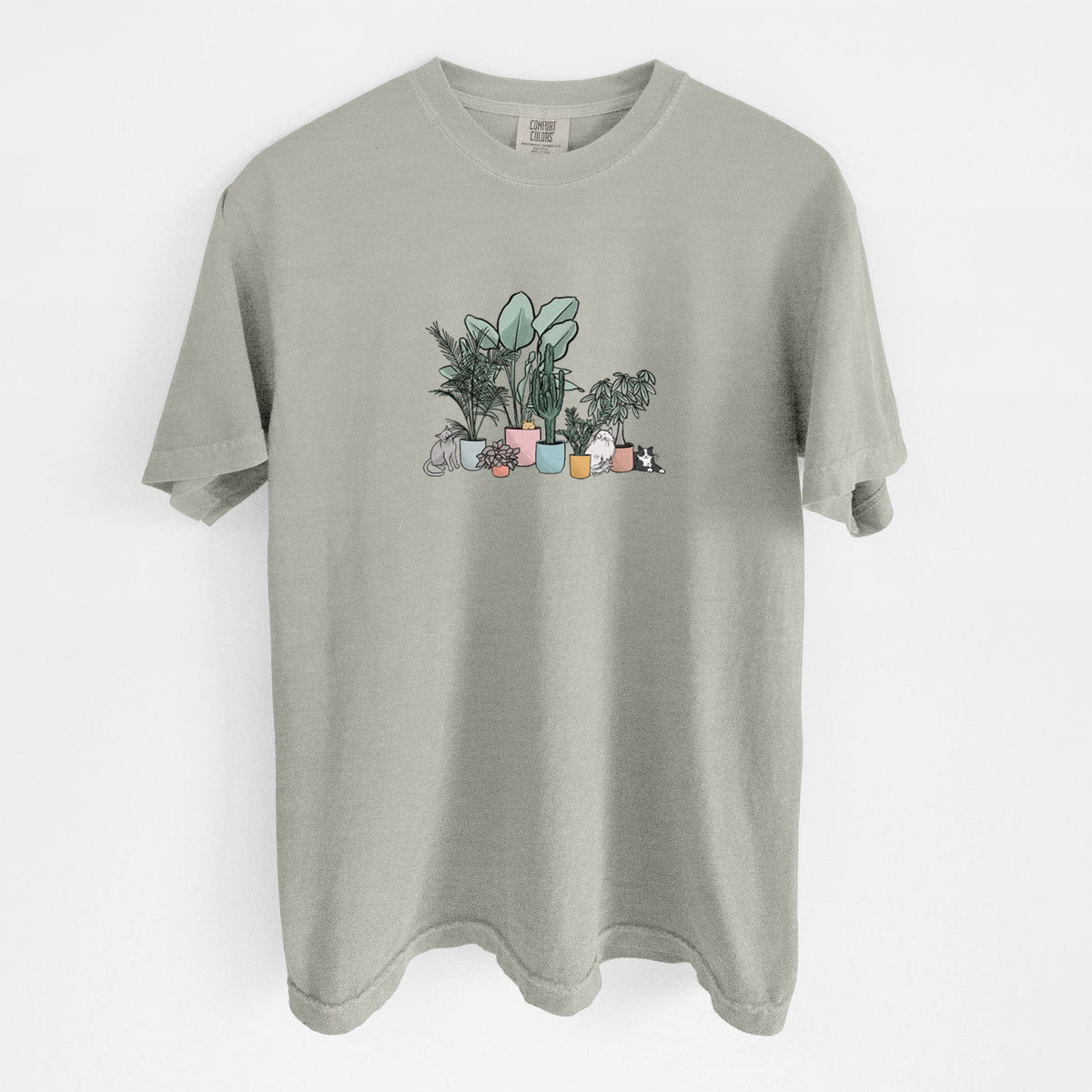 Sandstone beige Comfort Colors t-shirt laid flat, printed with a full-color illustration of cats lounging among potted houseplants.