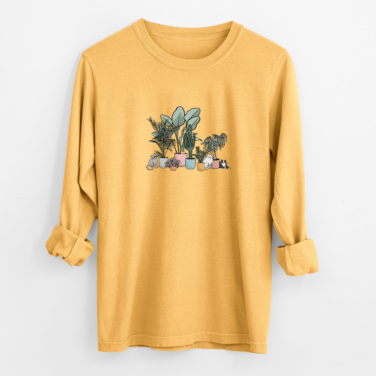 Golden wheat yellow Comfort Colors long sleeve shirt laid flat with the cuffs rolled, printed with a full-color illustration of cats lounging among potted houseplants.