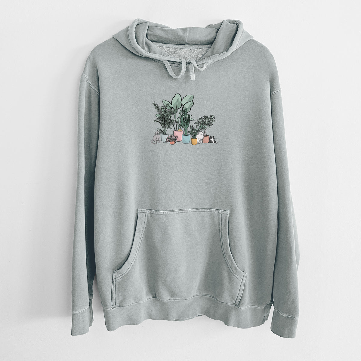 Sage green pigment dyed hoodie laid flat, printed with a full-color illustration of cats lounging among potted houseplants.