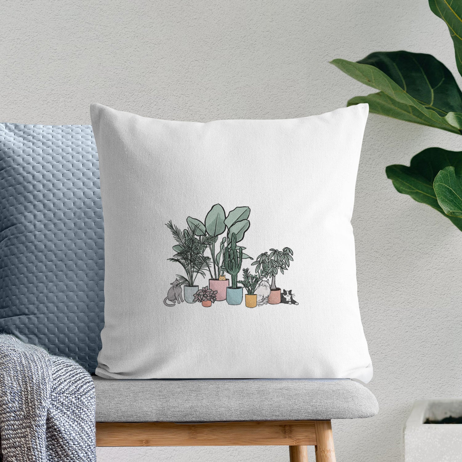 White pillow cover printed with a full-color illustration of cats lounging among potted houseplants, on a bench beside plants.