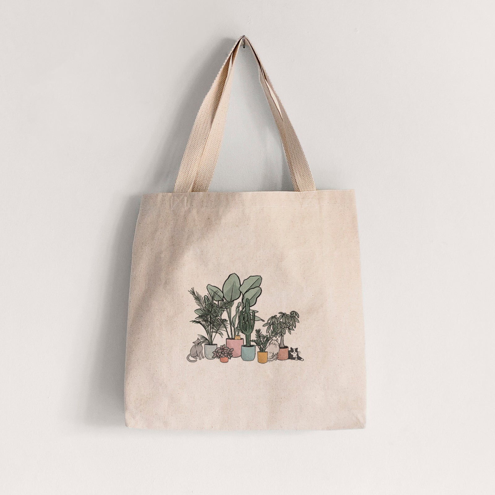 Natural canvas tote bag printed with a full-color illustration of cats lounging among potted houseplants.