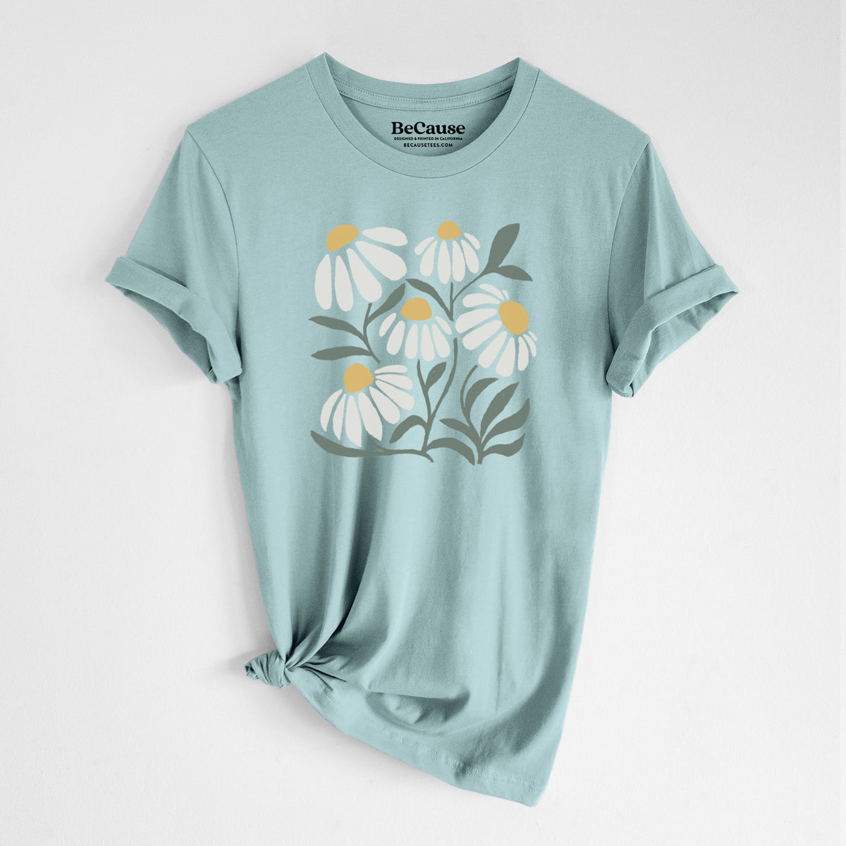 Dusty blue lightweight cotton t-shirt laid flat with the sleeves rolled, printed with a soft full-color illustration of white chamomile flowers and green leaves.