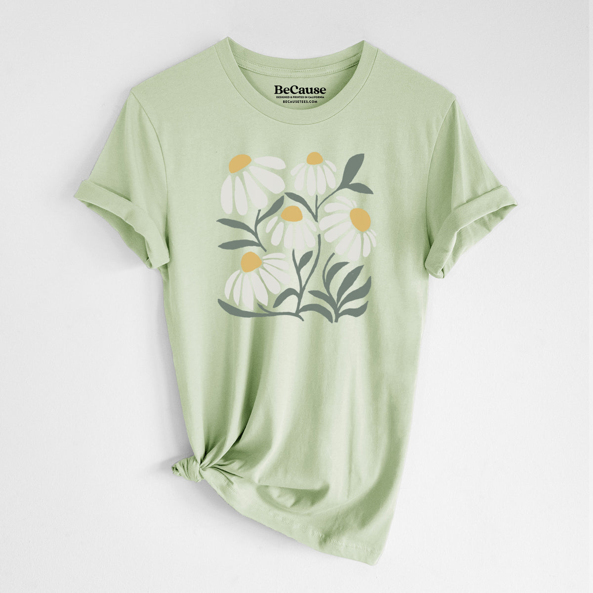 Spring green lightweight cotton t-shirt laid flat with the sleeves rolled, printed with a soft full-color illustration of white chamomile flowers and green leaves.