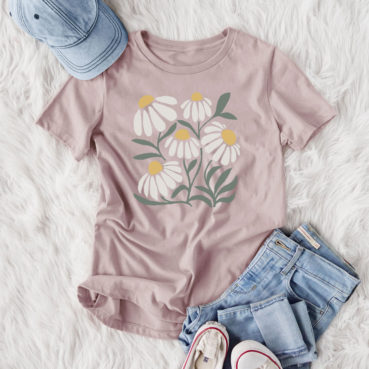 Women's relaxed fit cotton t-shirt printed with a soft full-color illustration of white chamomile flowers and green leaves, styled flat on a white faux fur rug with jeans.