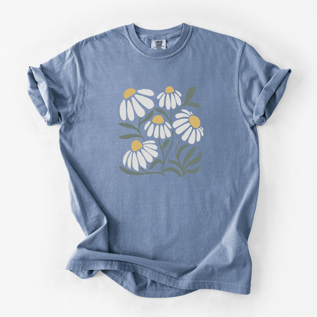 Blue jean Comfort Colors t-shirt laid flat, printed with a soft full-color illustration of white chamomile flowers and green leaves.