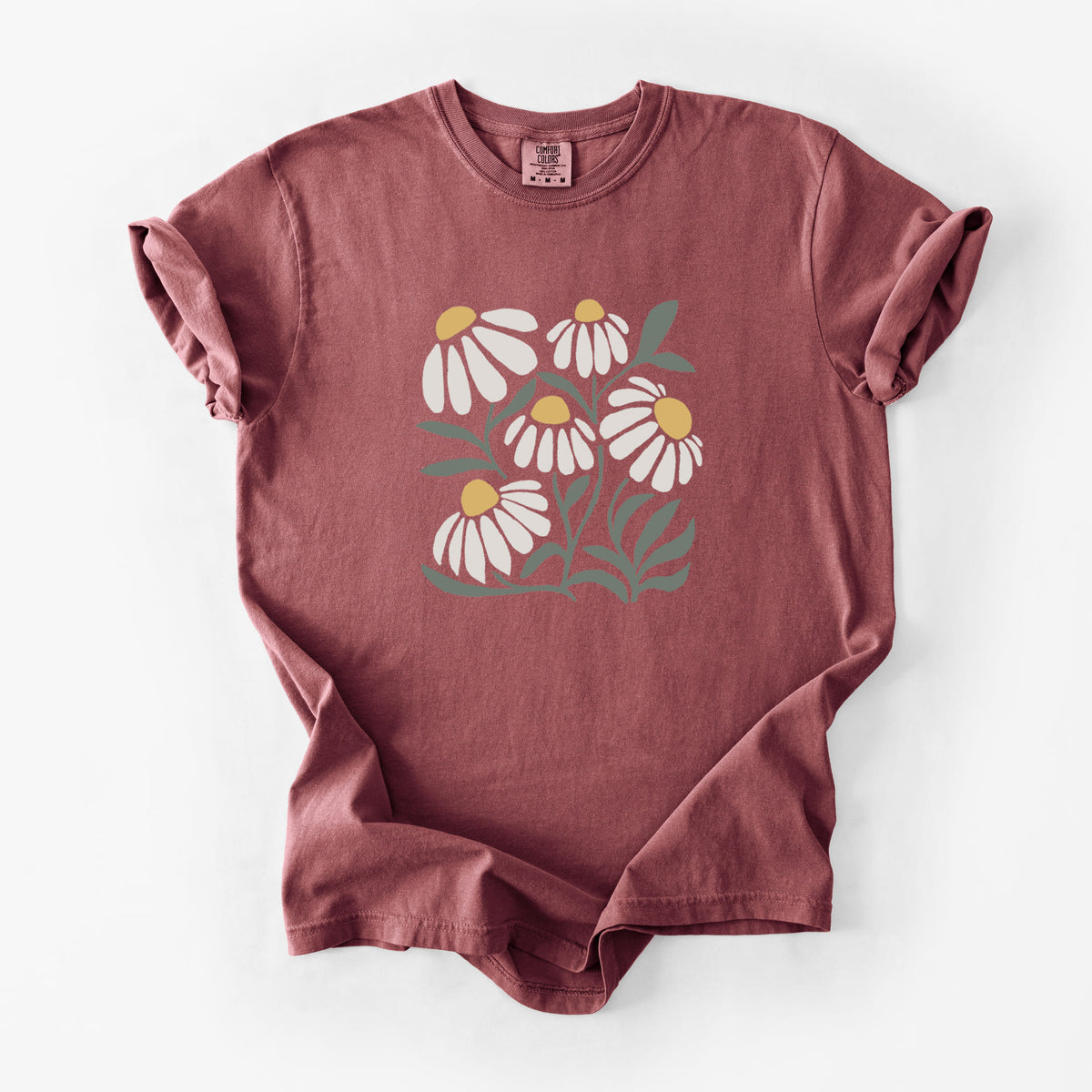 Brick red Comfort Colors t-shirt laid flat, printed with a soft full-color illustration of white chamomile flowers and green leaves.