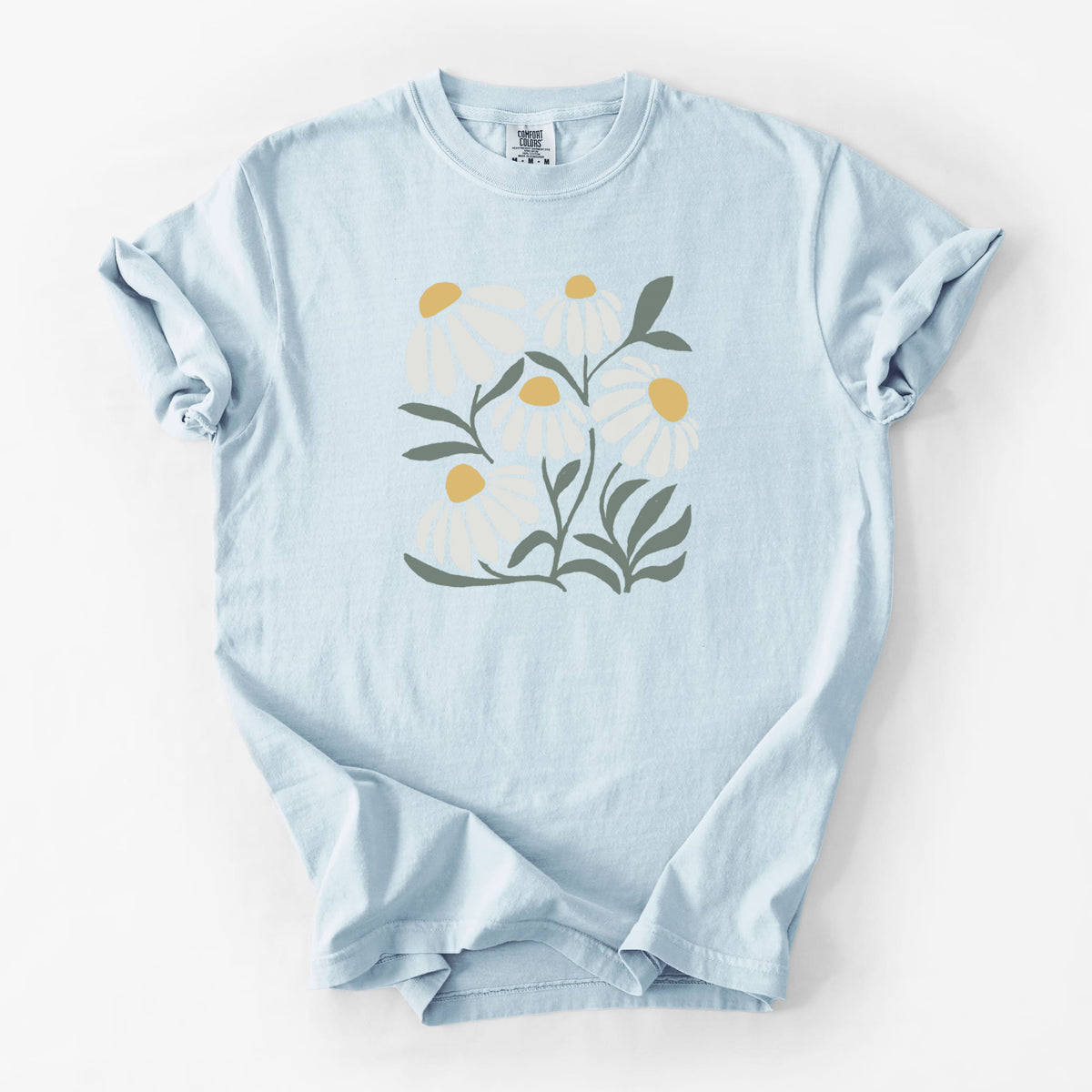 Chambray blue Comfort Colors t-shirt laid flat, printed with a soft full-color illustration of white chamomile flowers and green leaves.