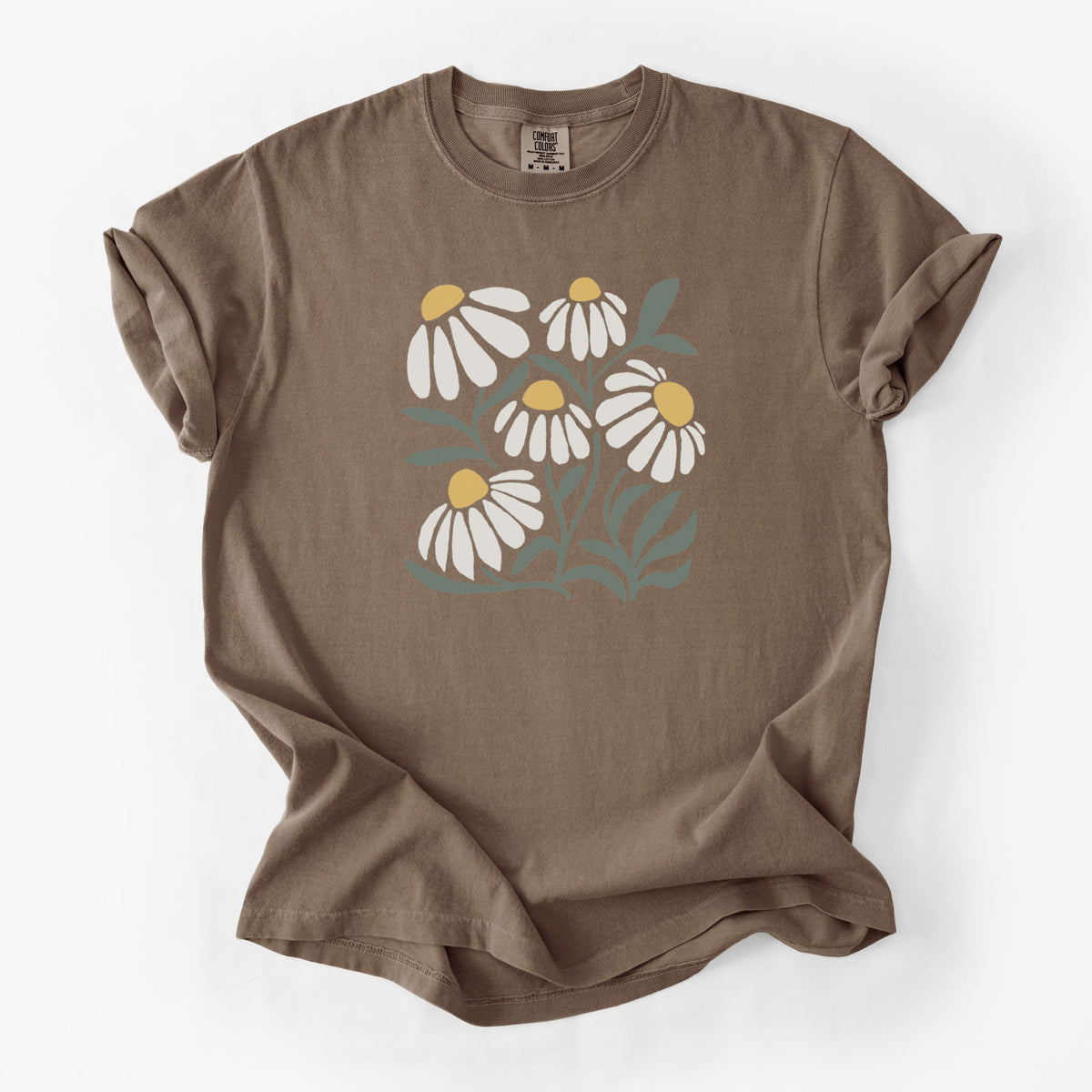 Espresso brown Comfort Colors t-shirt laid flat, printed with a soft full-color illustration of white chamomile flowers and green leaves.