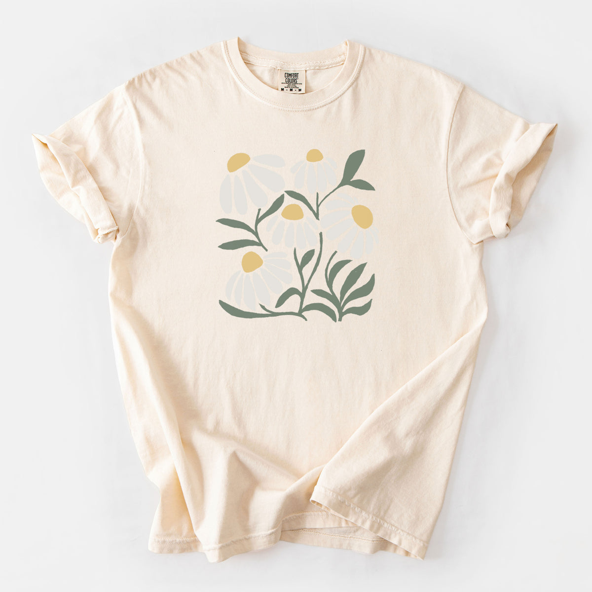 Ivory Comfort Colors t-shirt laid flat, printed with a soft full-color illustration of white chamomile flowers and green leaves.