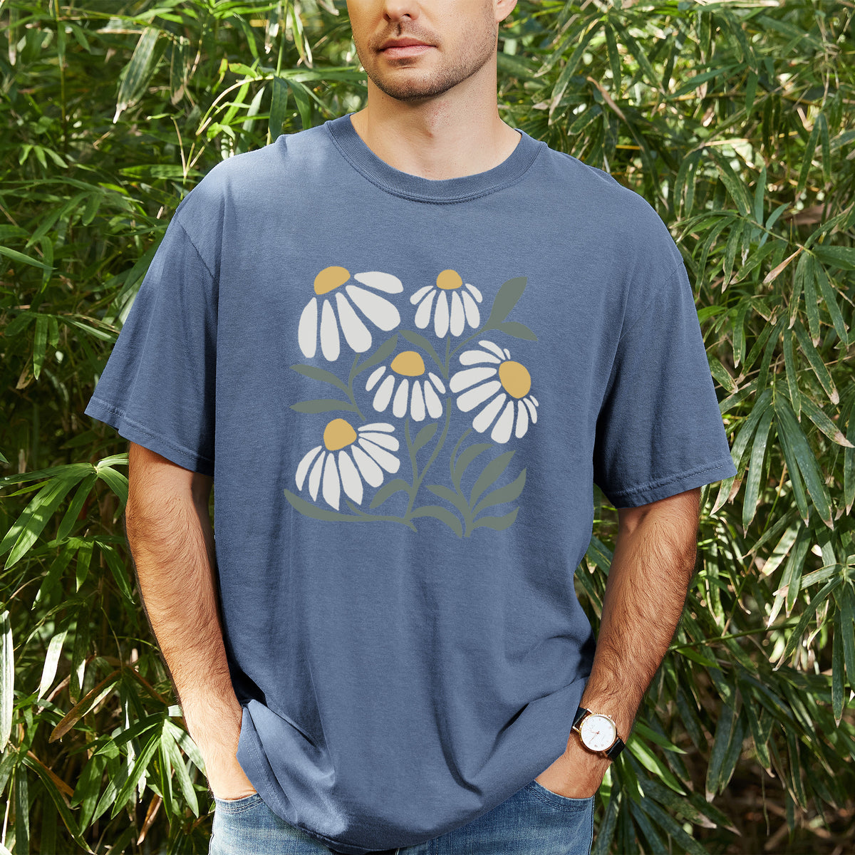 Man wearing a Comfort Colors t-shirt printed with a soft full-color illustration of white chamomile flowers and green leaves, outdoors.