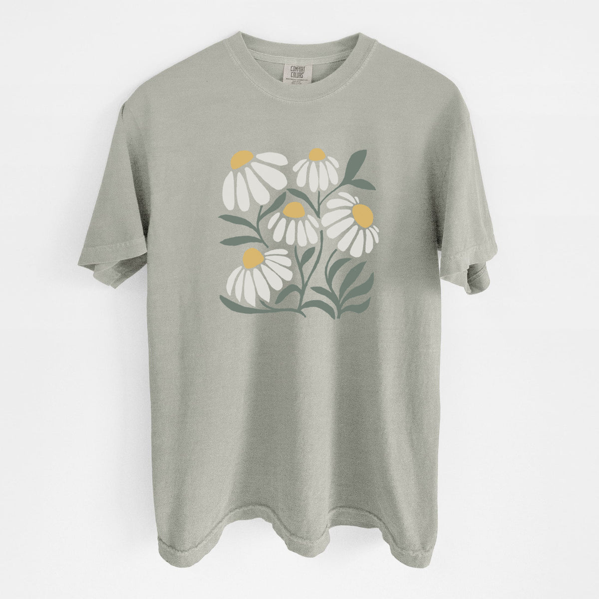 Sandstone beige Comfort Colors t-shirt laid flat, printed with a soft full-color illustration of white chamomile flowers and green leaves.