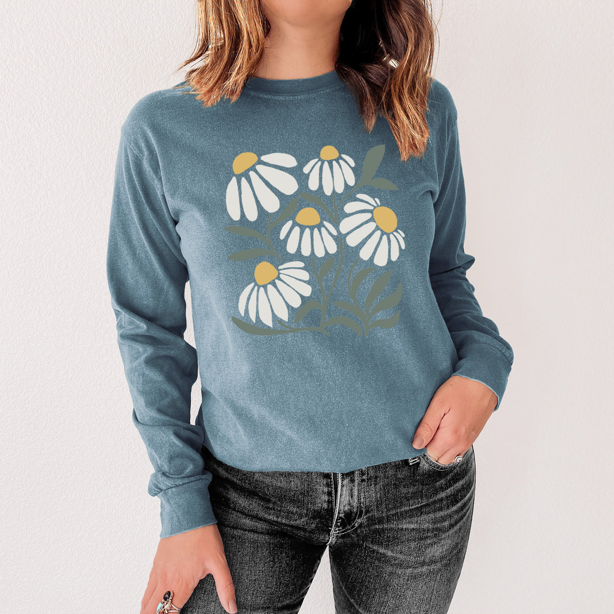 Steel blue Comfort Colors long sleeve shirt printed with a soft full-color illustration of white chamomile flowers and green leaves, shown in a lifestyle photo.