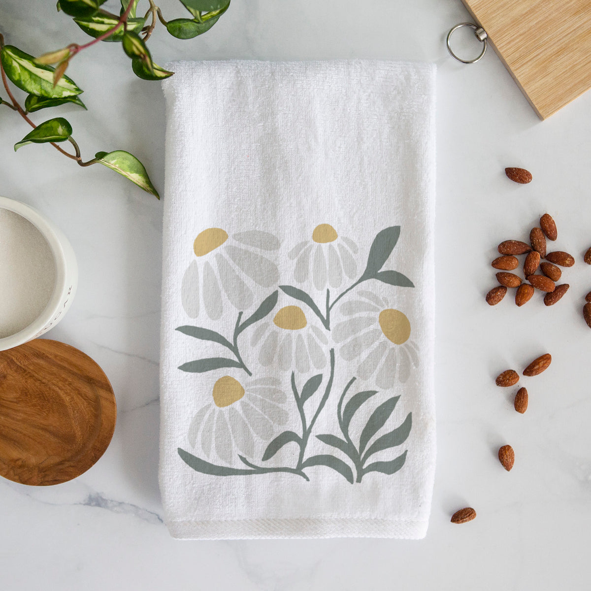 White hand towel printed with a soft full-color illustration of white chamomile flowers and green leaves.