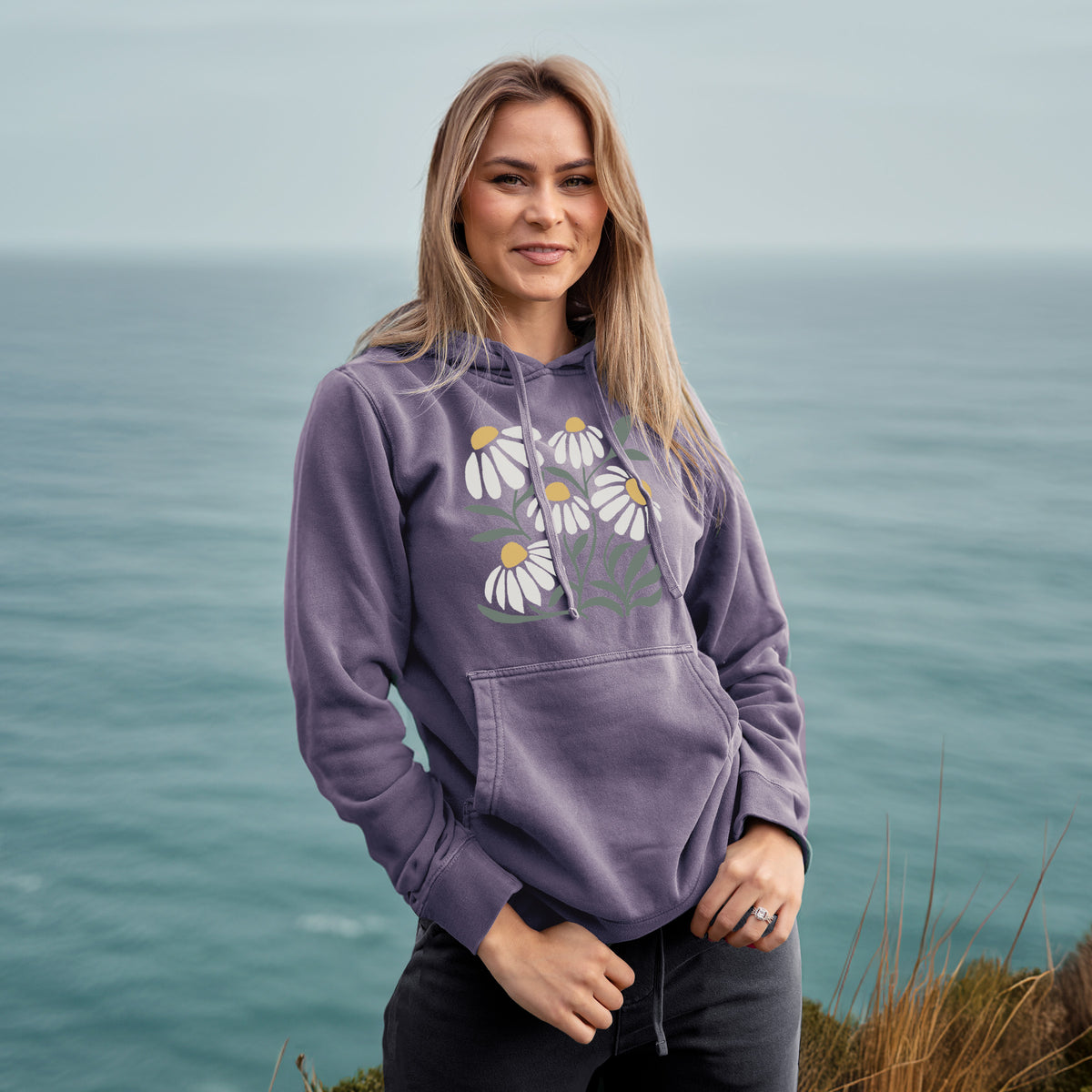 Woman wearing a plum purple pigment dyed hoodie printed with a soft full-color illustration of white chamomile flowers and green leaves.