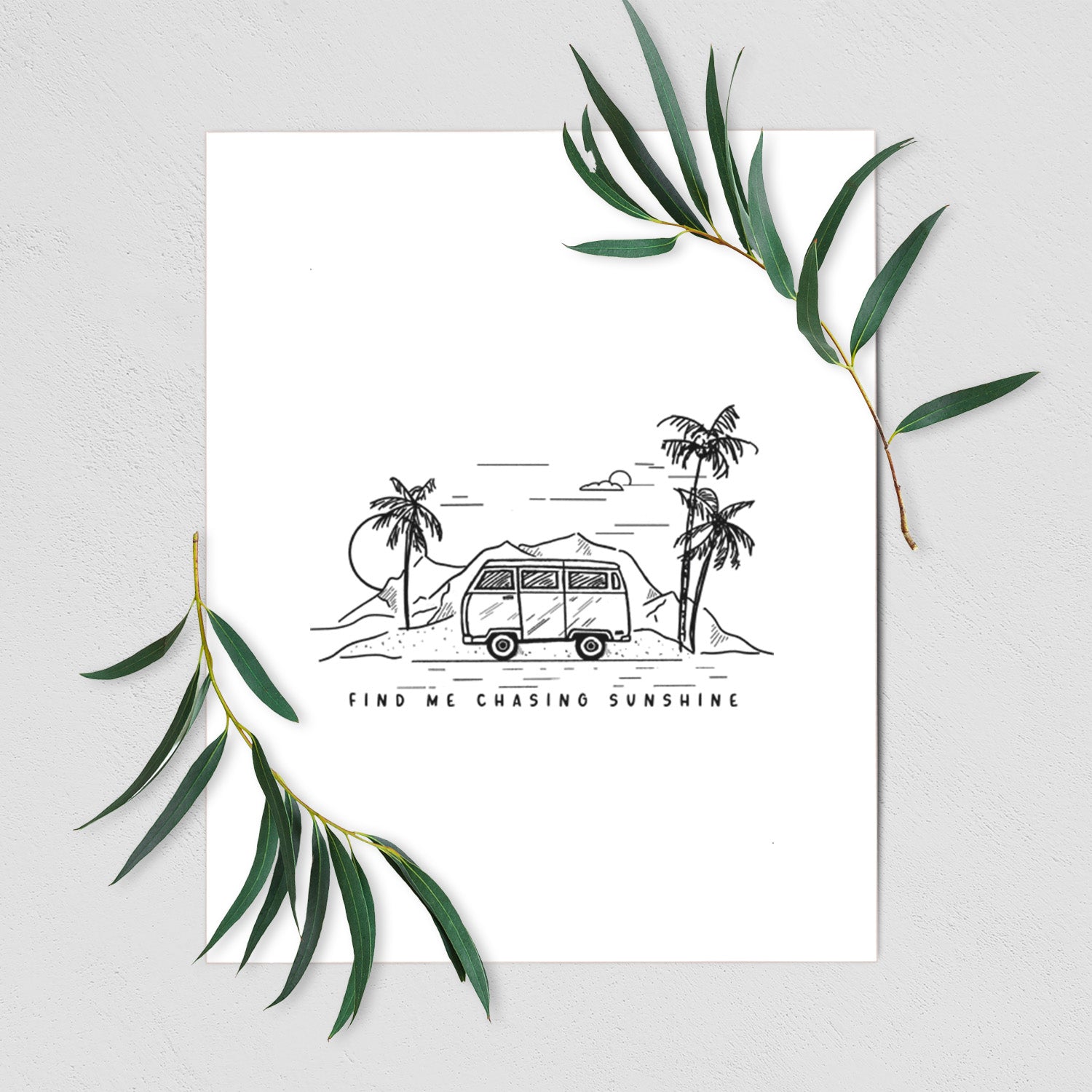 Art print of a black ink illustration of a camper van under palm trees and the sun, with the words Find Me Chasing Sunshine, shown with eucalyptus leaves.
