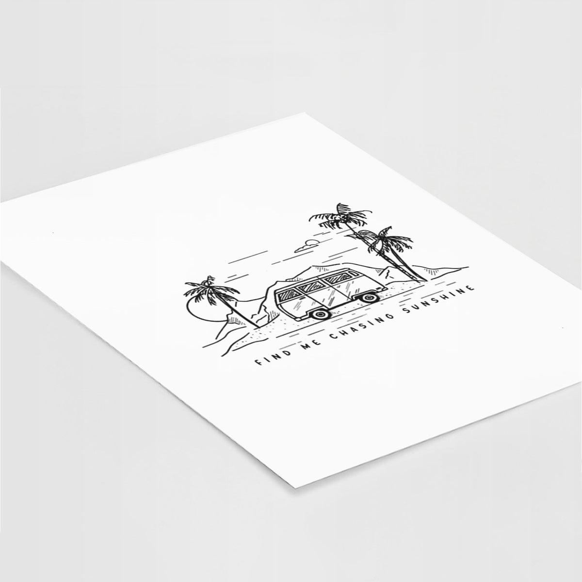 Art print of a black ink illustration of a camper van under palm trees and the sun, with the words Find Me Chasing Sunshine, lying at an angle on a white surface.