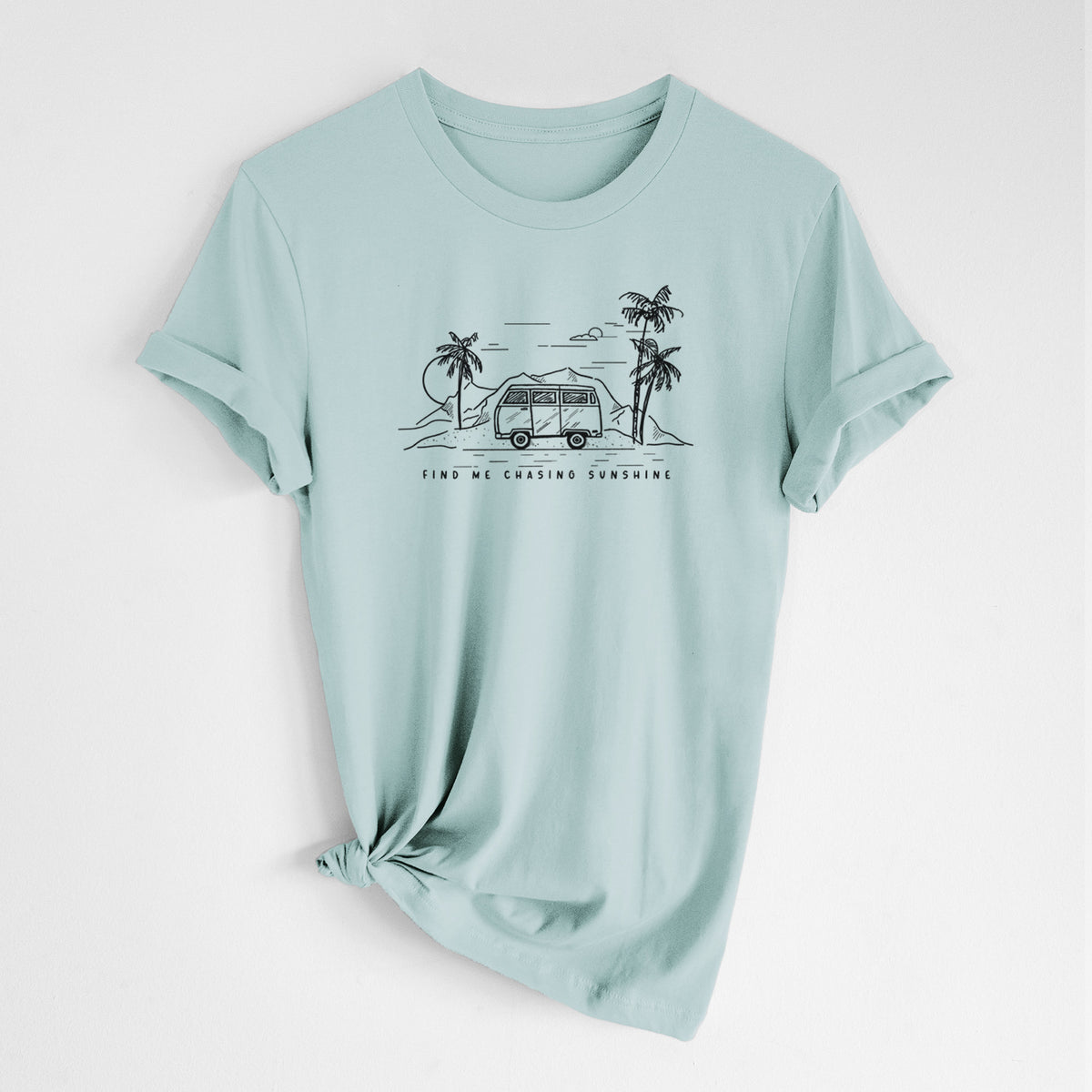Dusty blue lightweight cotton t-shirt laid flat with the sleeves rolled, printed with a black ink illustration of a camper van under palm trees and the sun, with the words Find Me Chasing Sunshine.