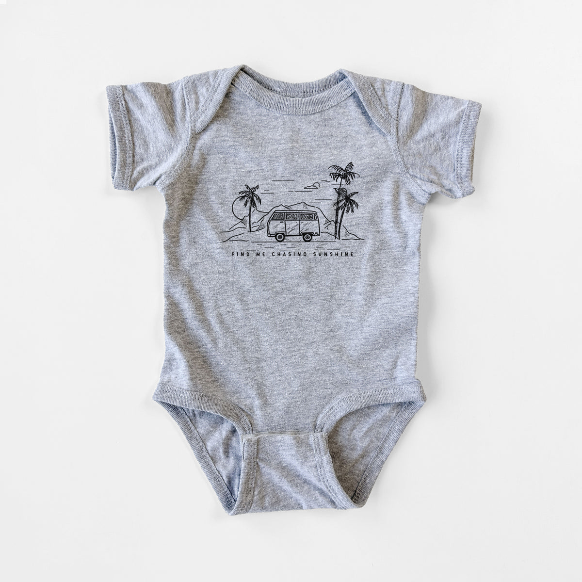 Grey baby bodysuit laid flat, printed with a black ink illustration of a camper van under palm trees and the sun, with the words Find Me Chasing Sunshine.