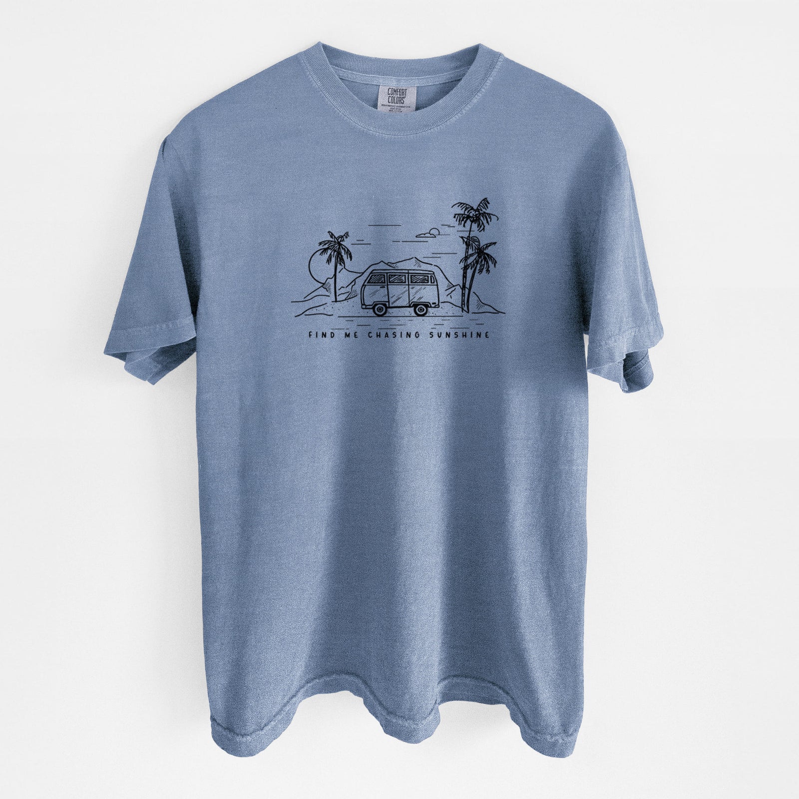 Blue jean Comfort Colors t-shirt laid flat, printed with a black ink illustration of a camper van under palm trees and the sun, with the words Find Me Chasing Sunshine.
