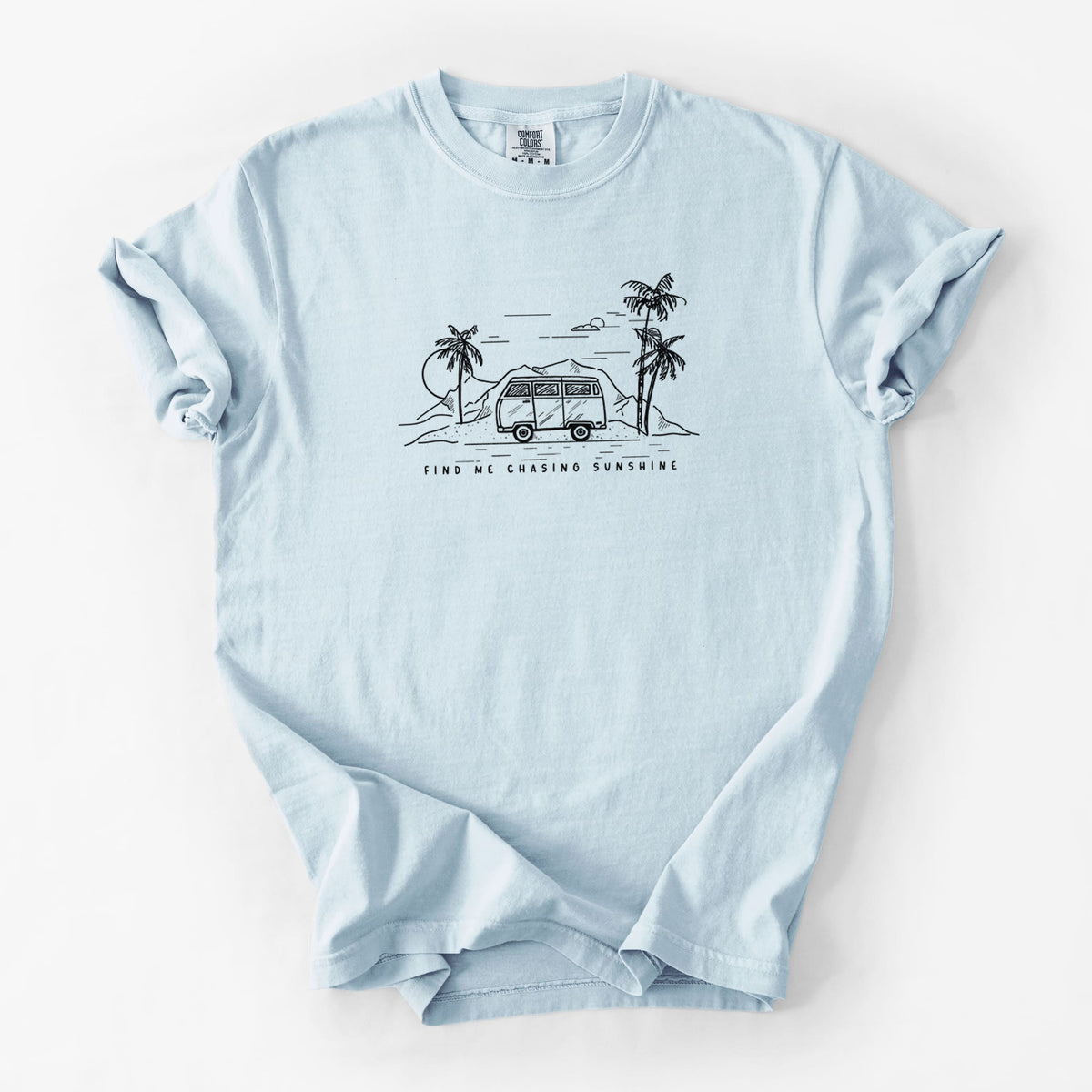 Chambray blue Comfort Colors t-shirt laid flat, printed with a black ink illustration of a camper van under palm trees and the sun, with the words Find Me Chasing Sunshine.