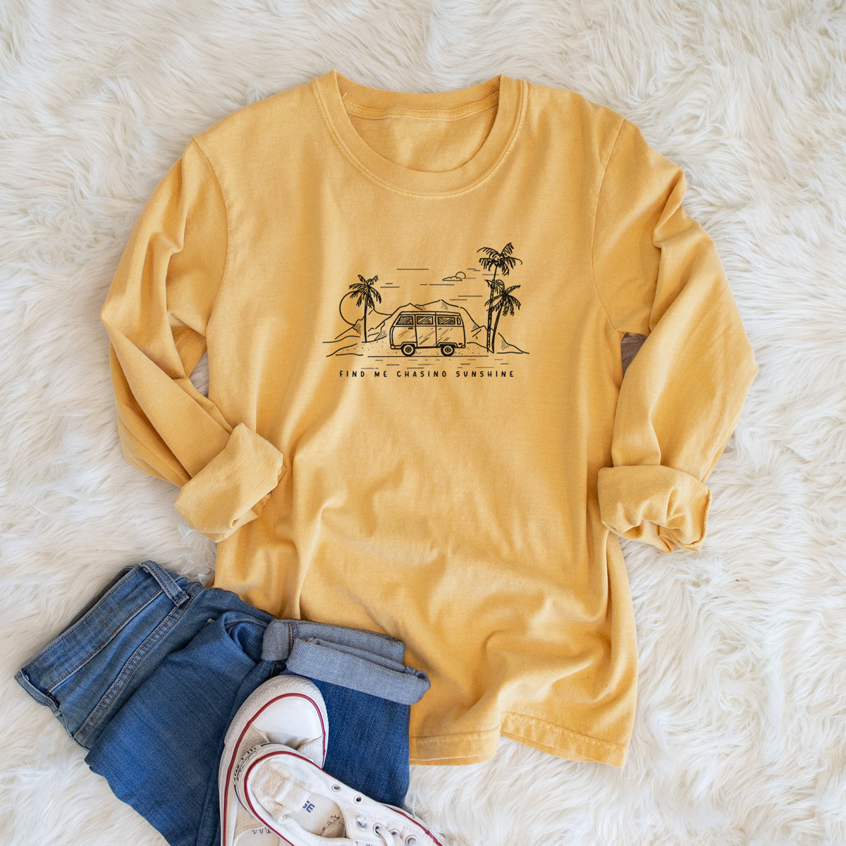 Golden wheat yellow Comfort Colors long sleeve shirt printed with a black ink illustration of a camper van under palm trees and the sun, with the words Find Me Chasing Sunshine, shown in a lifestyle photo.