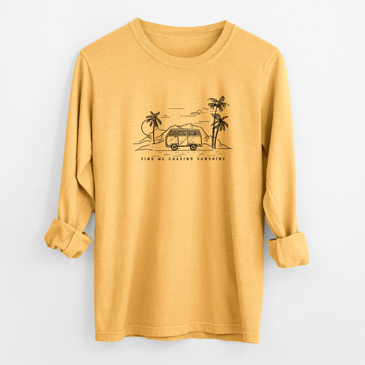 Golden wheat yellow Comfort Colors long sleeve shirt laid flat with the cuffs rolled, printed with a black ink illustration of a camper van under palm trees and the sun, with the words Find Me Chasing Sunshine.
