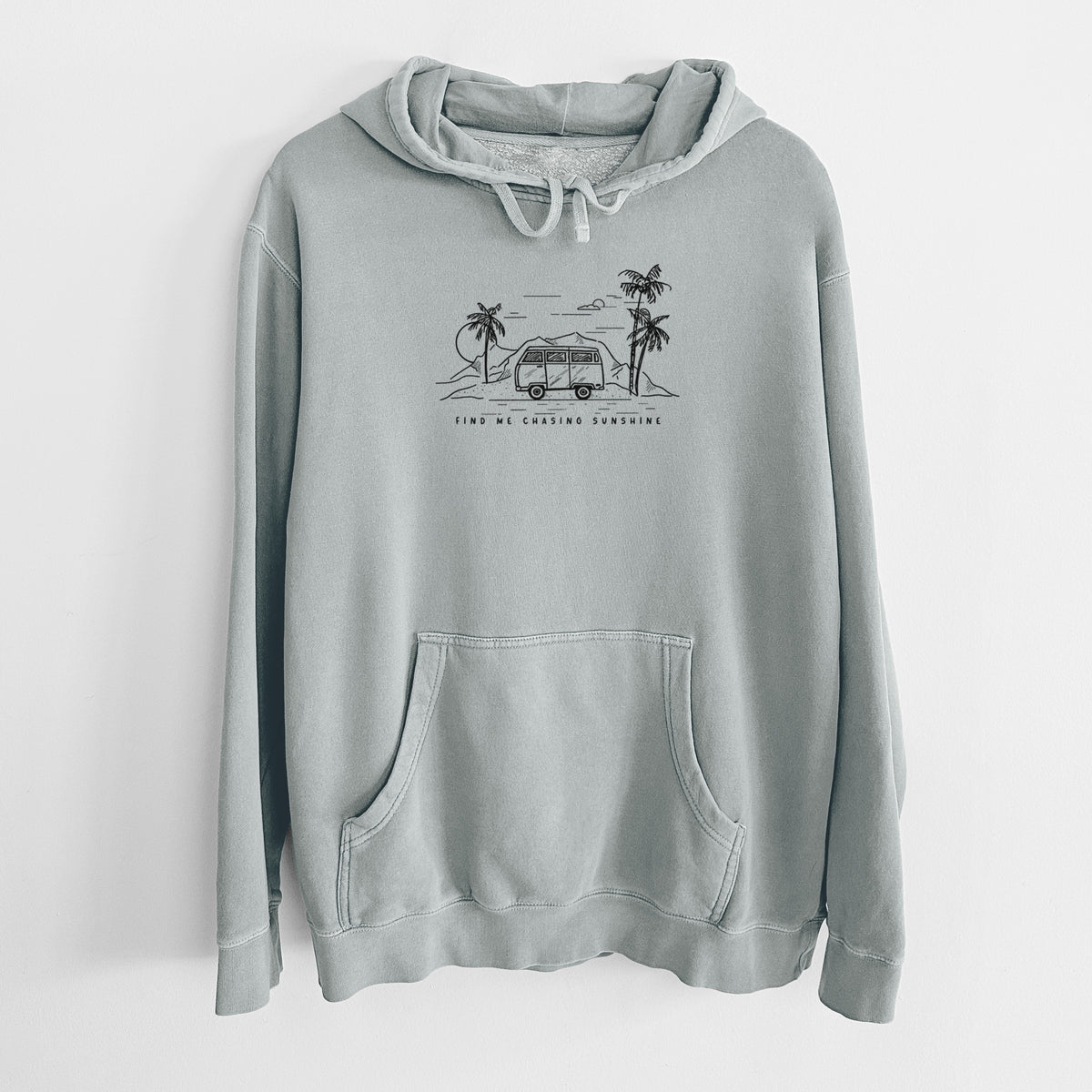 Sage green pigment dyed hoodie laid flat, printed with a black ink illustration of a camper van under palm trees and the sun, with the words Find Me Chasing Sunshine.