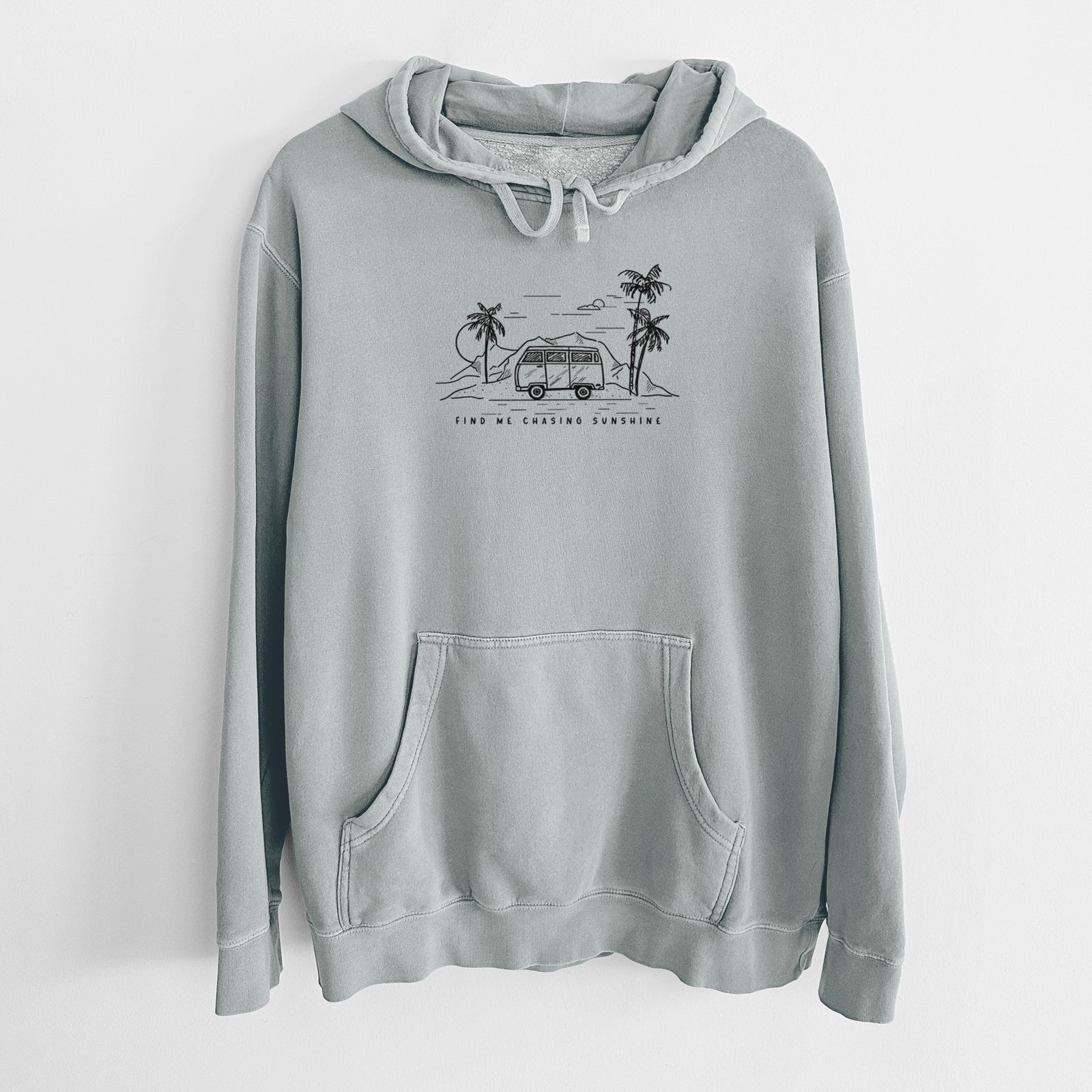 Sage green pigment dyed hoodie laid flat, printed with a black ink illustration of a camper van under palm trees and the sun, with the words Find Me Chasing Sunshine.