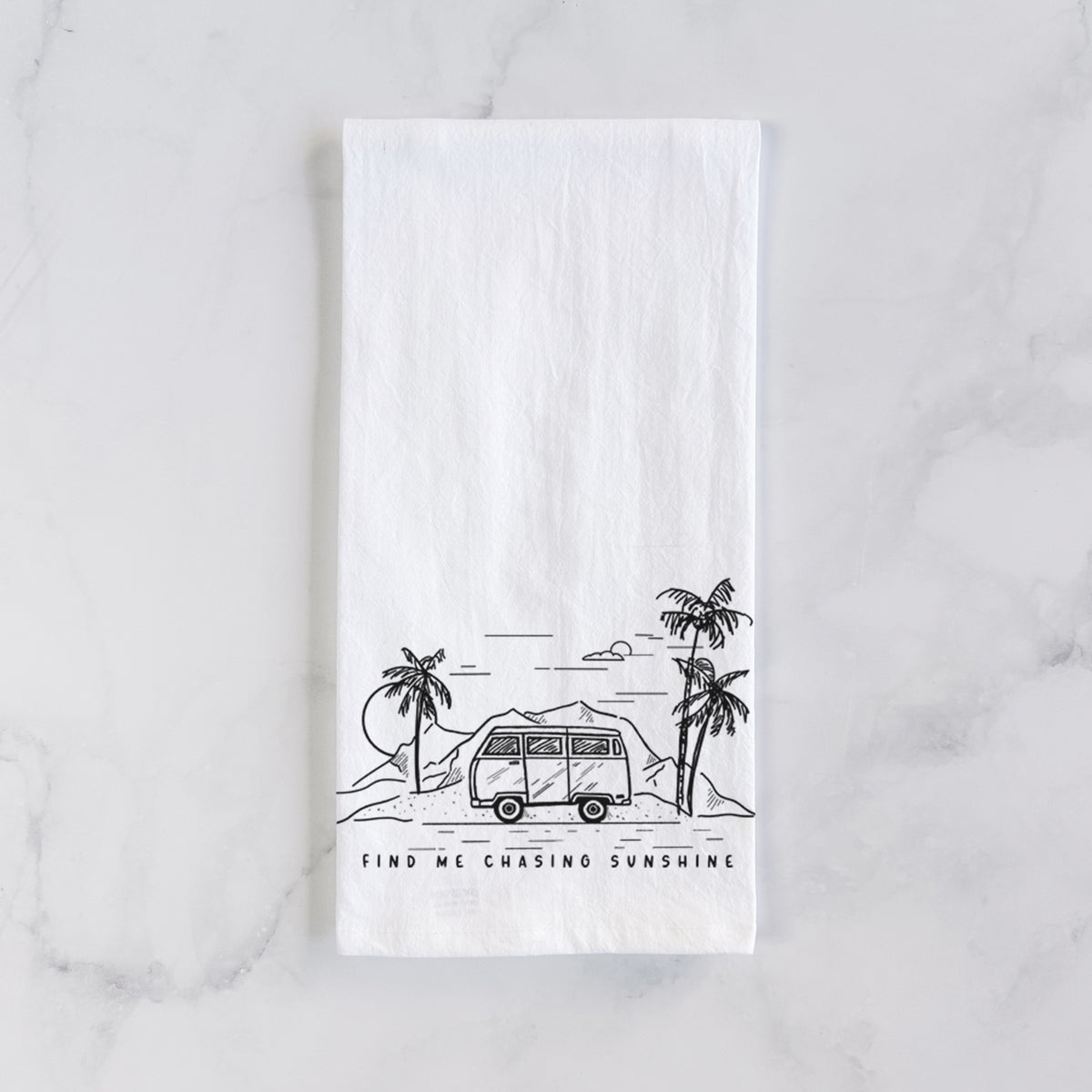 White cotton tea towel laid flat on marble, printed with a black ink illustration of a camper van under palm trees and the sun, with the words Find Me Chasing Sunshine.