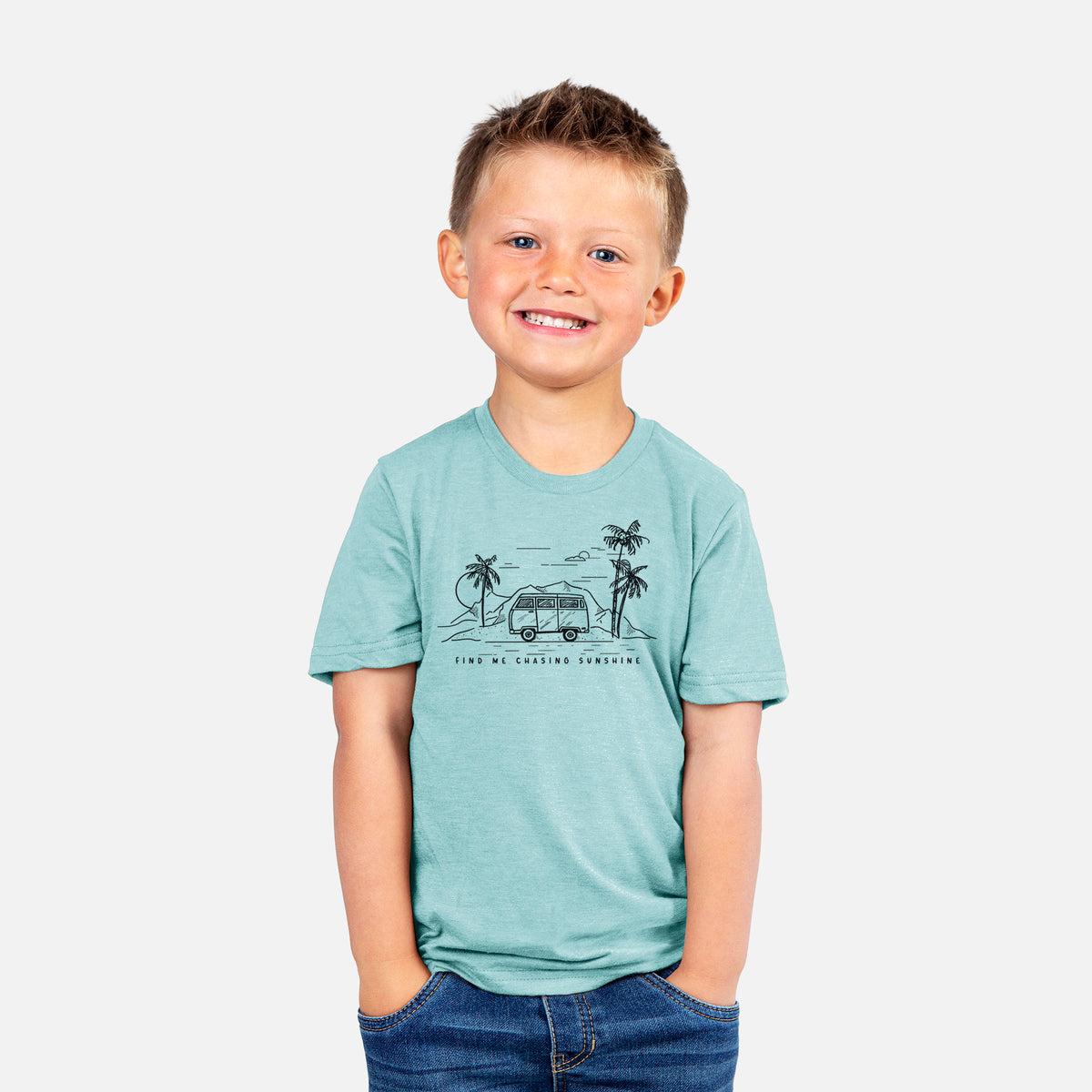 Smiling boy wearing a youth t-shirt printed with a black ink illustration of a camper van under palm trees and the sun, with the words Find Me Chasing Sunshine.