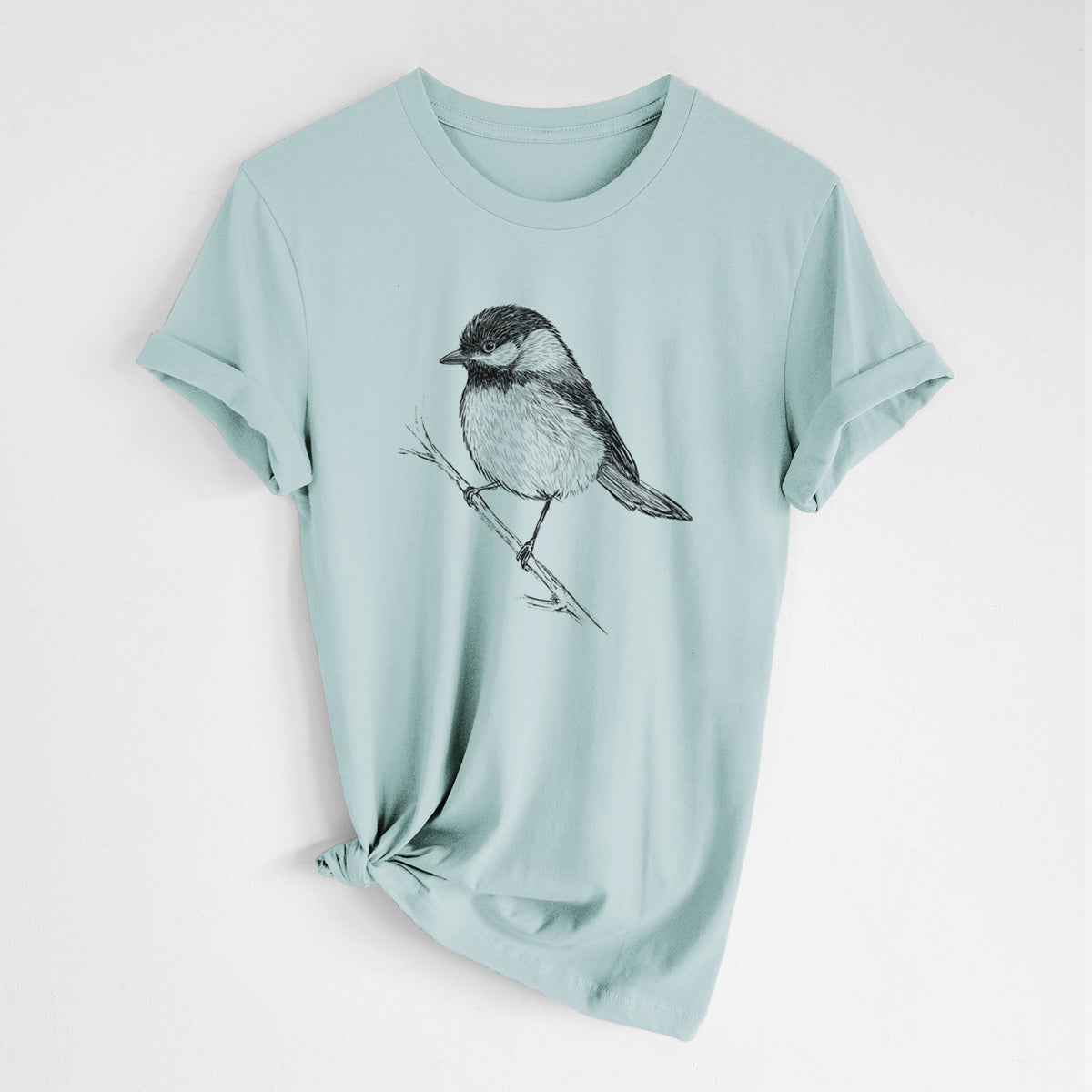 Dusty blue lightweight cotton t-shirt laid flat with the sleeves rolled, printed with a detailed black ink sketch of a black-capped chickadee perched on a branch.