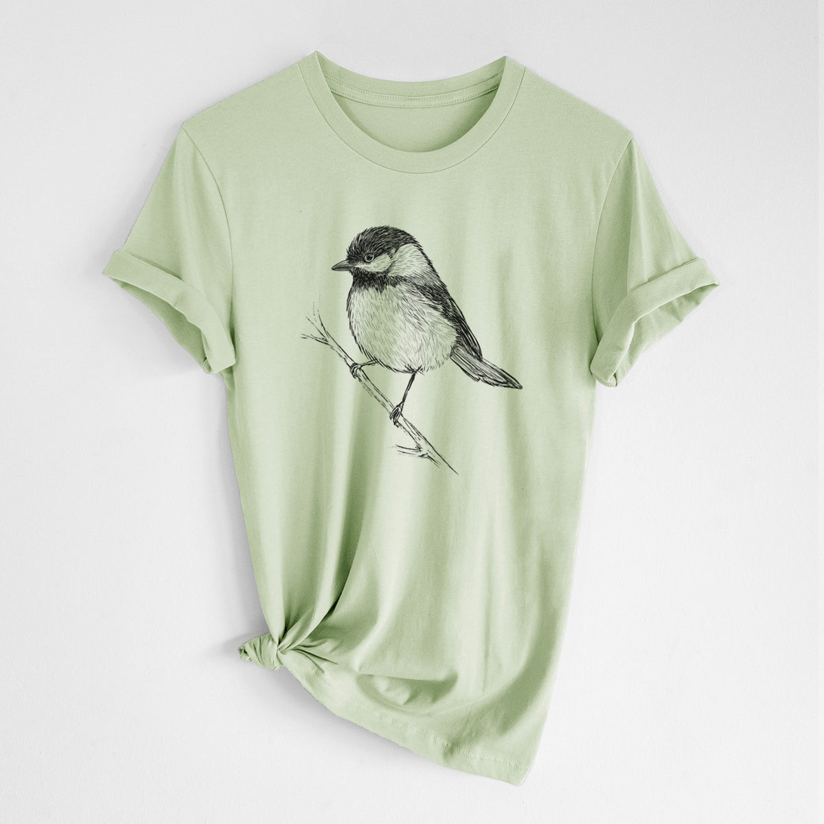 Spring green lightweight cotton t-shirt laid flat with the sleeves rolled, printed with a detailed black ink sketch of a black-capped chickadee perched on a branch.