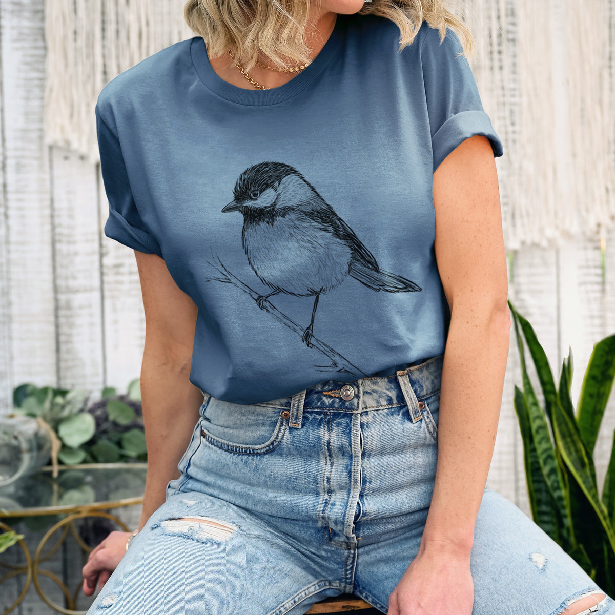 Woman wearing a steel blue lightweight cotton t-shirt printed with a detailed black ink sketch of a black-capped chickadee perched on a branch.