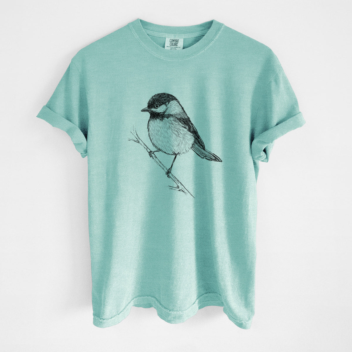 Chalky mint Comfort Colors t-shirt laid flat, printed with a detailed black ink sketch of a black-capped chickadee perched on a branch.