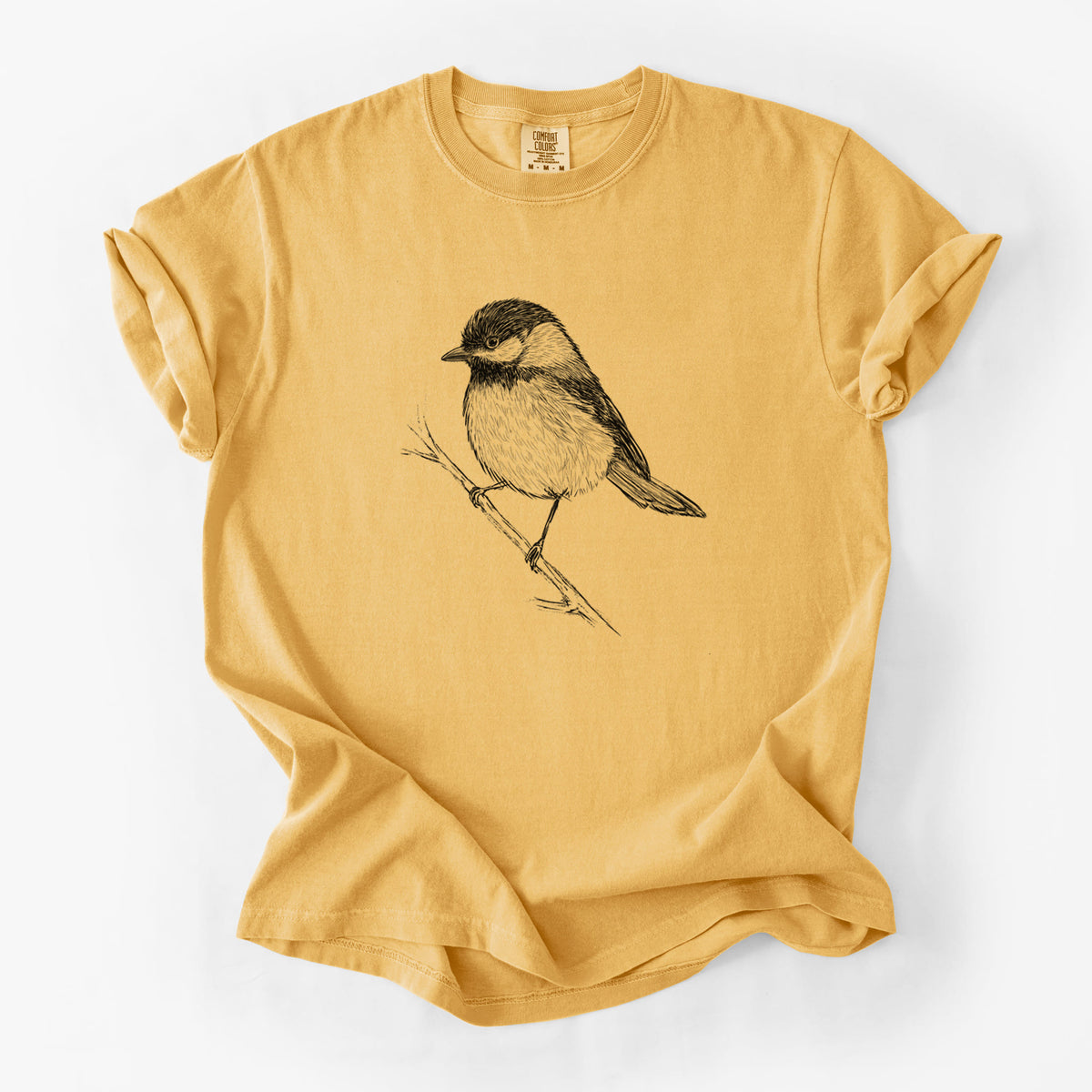 Golden wheat yellow Comfort Colors t-shirt laid flat, printed with a detailed black ink sketch of a black-capped chickadee perched on a branch.