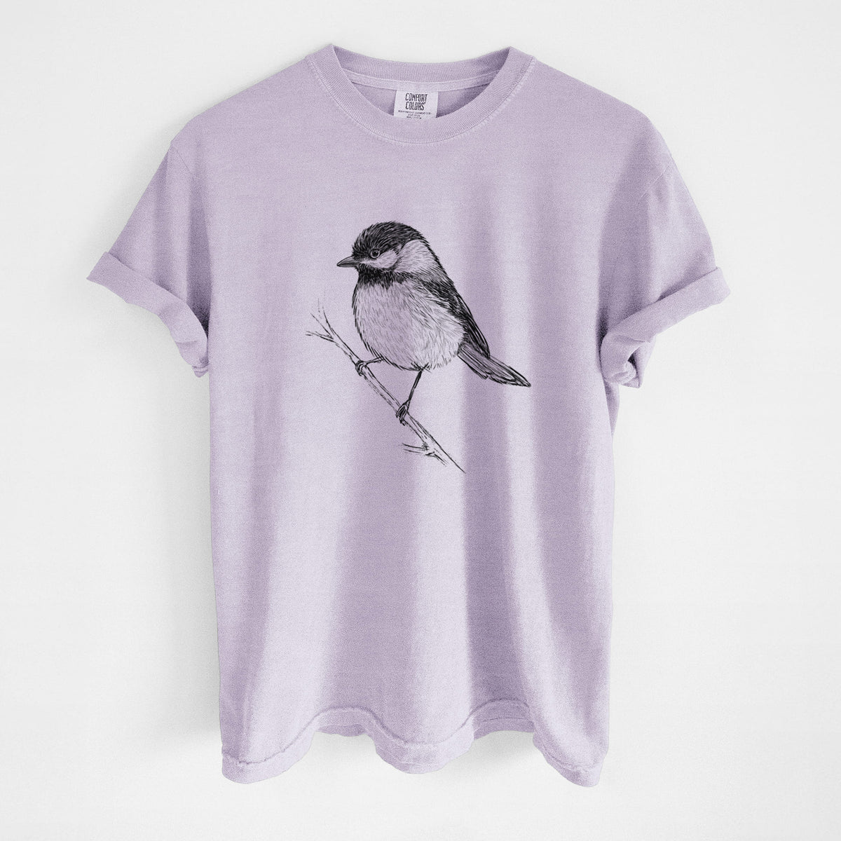 Orchid purple Comfort Colors t-shirt laid flat, printed with a detailed black ink sketch of a black-capped chickadee perched on a branch.